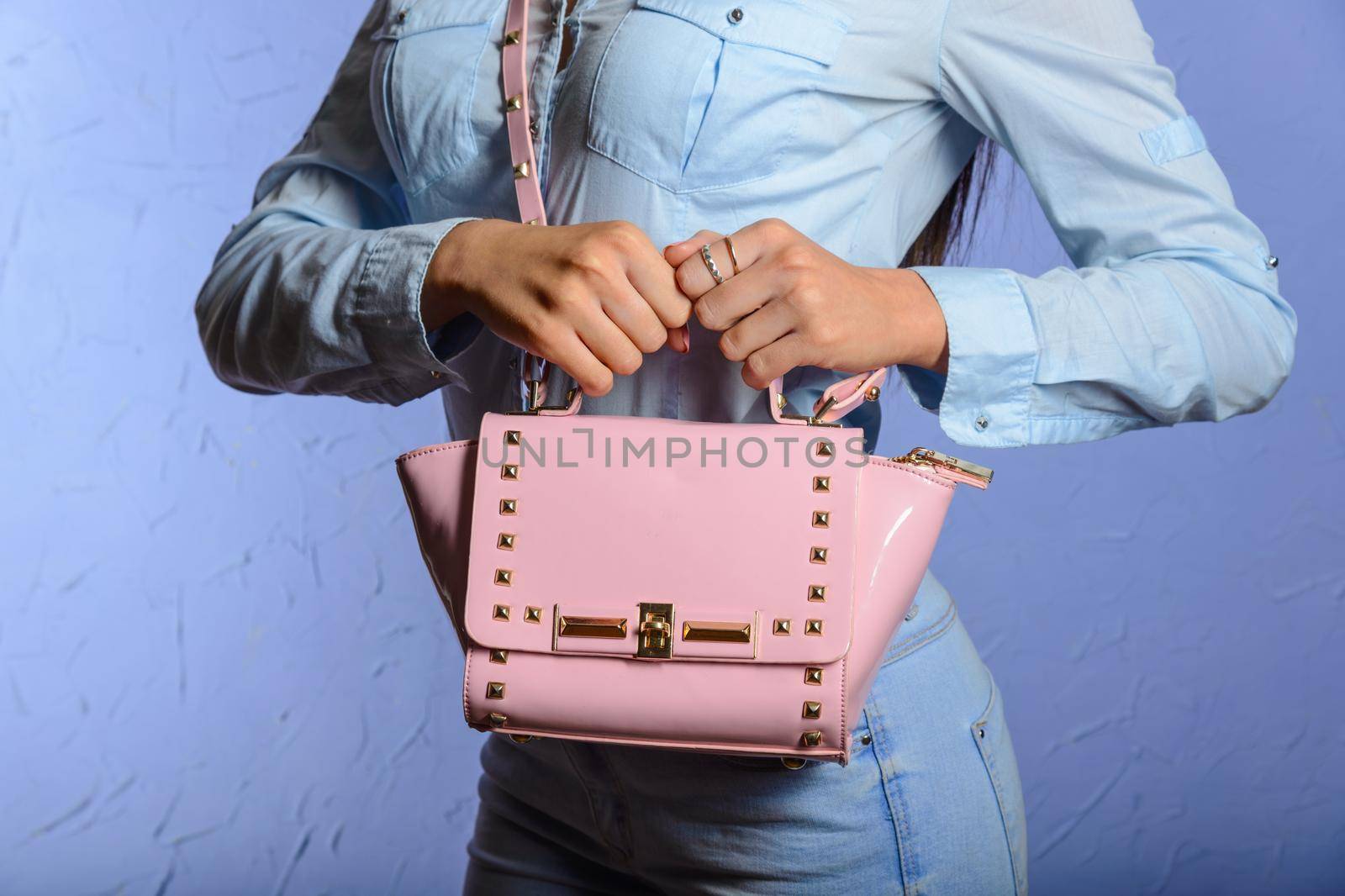 trendy woman in jeans and denim shirt with pink handbag in hands beige background