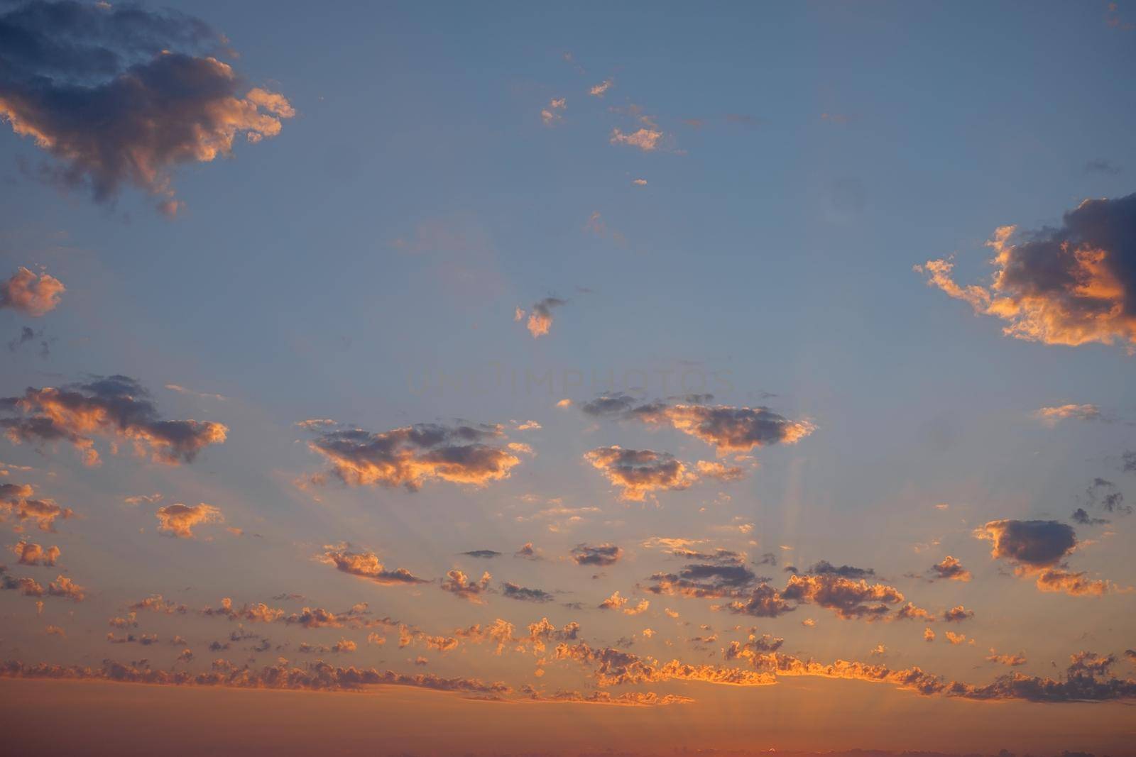 Sky background, beautiful sunset with sunbeams among small clouds.