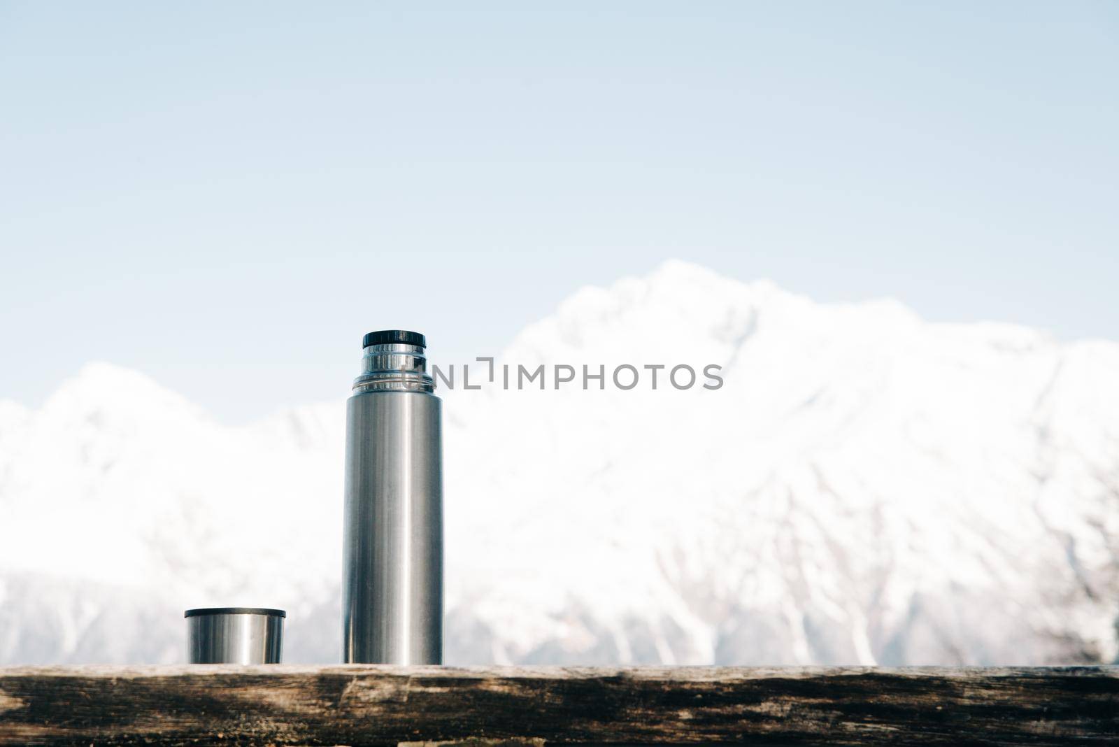 Thermos with cup on a wooden table on background of snowy mountains in winter.