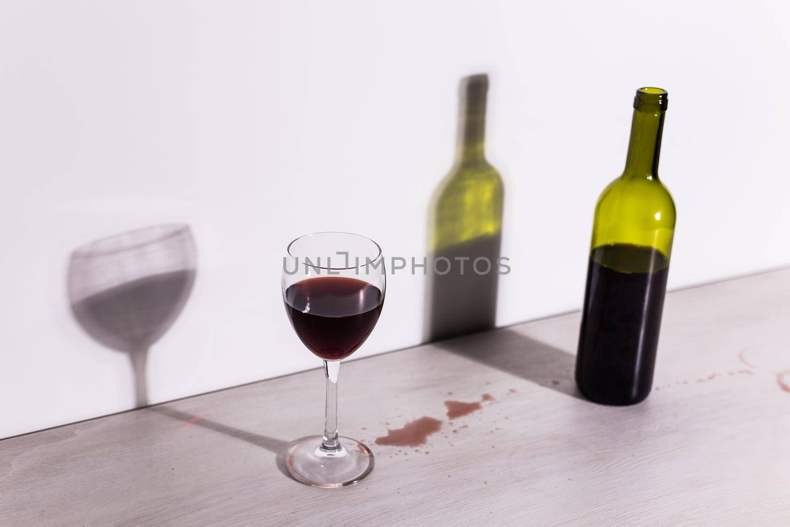 Bottle with wine and glass, red puddle of wine on the table. Cleaning after party concept