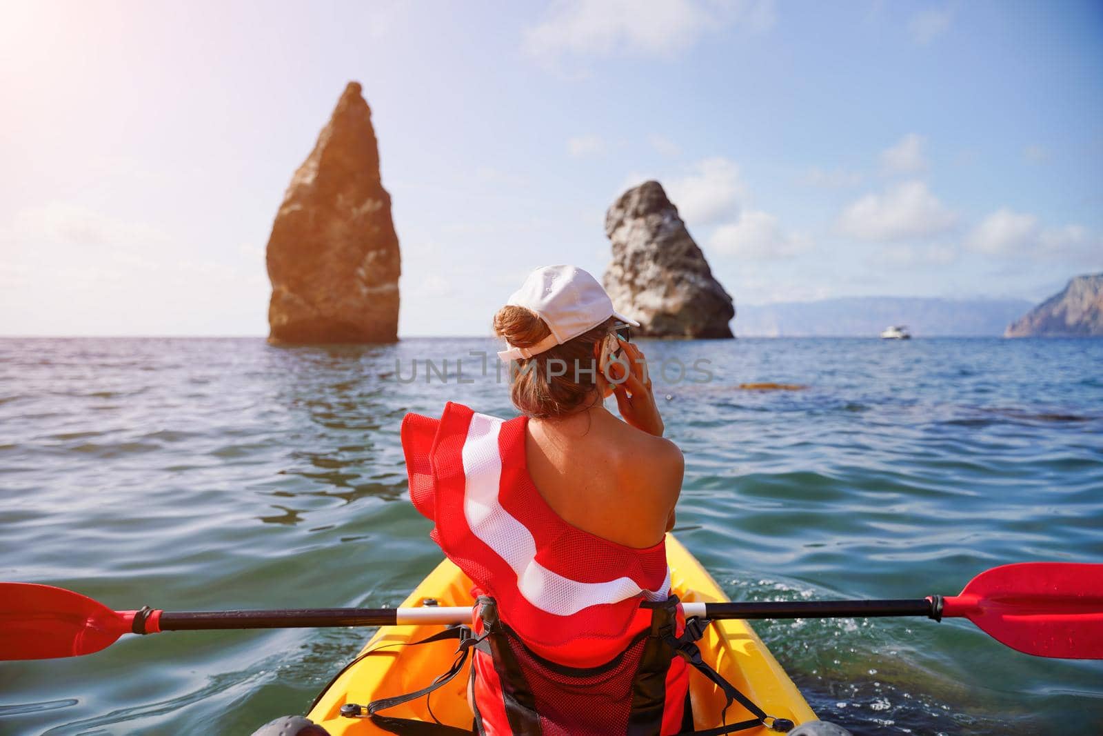 Young brunette woman in red swimsuit and Santa hat, swimming on kayak around basalt rocks like in Iceland. Back view. Christmas and travel concept