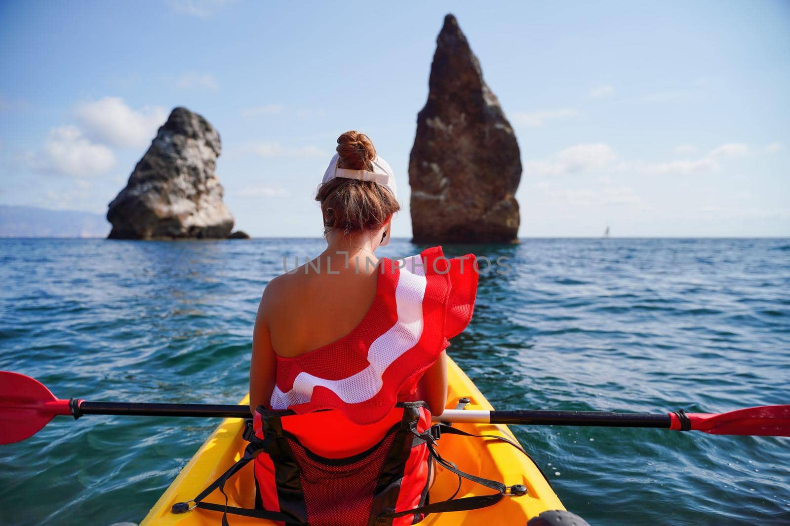 Young attractive brunette woman in red swimsuit, swimming on kayak around volcanic rocks, like in Iceland. Back view. Christmas holiday vacation and travel concept. by panophotograph