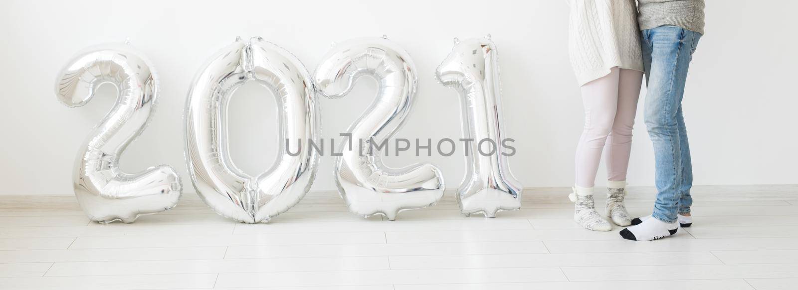 Holidays, festive and party concept - Happy loving couple holds silver 2021 balloons on white background. New Year celebration. by Satura86