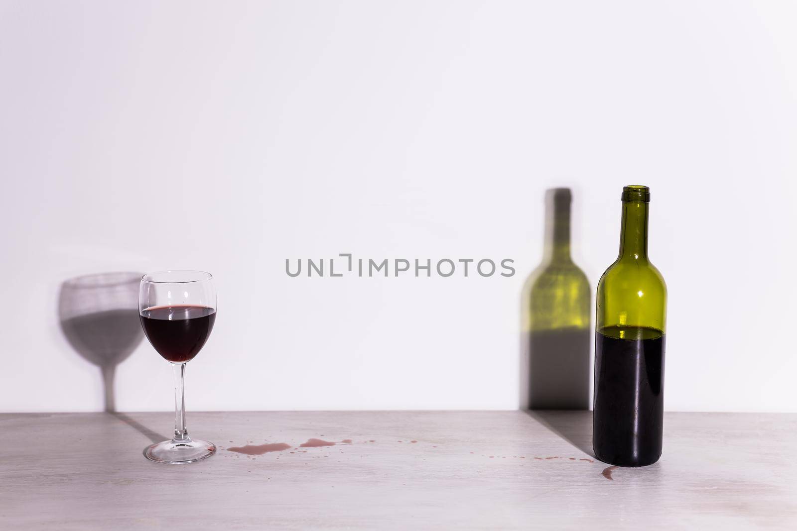 Bottle with wine and glass, red puddle of wine on the table. Cleaning after party concept