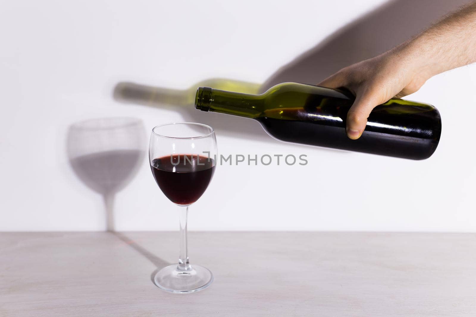 Pouring red wine into the glass against wooden background by Satura86