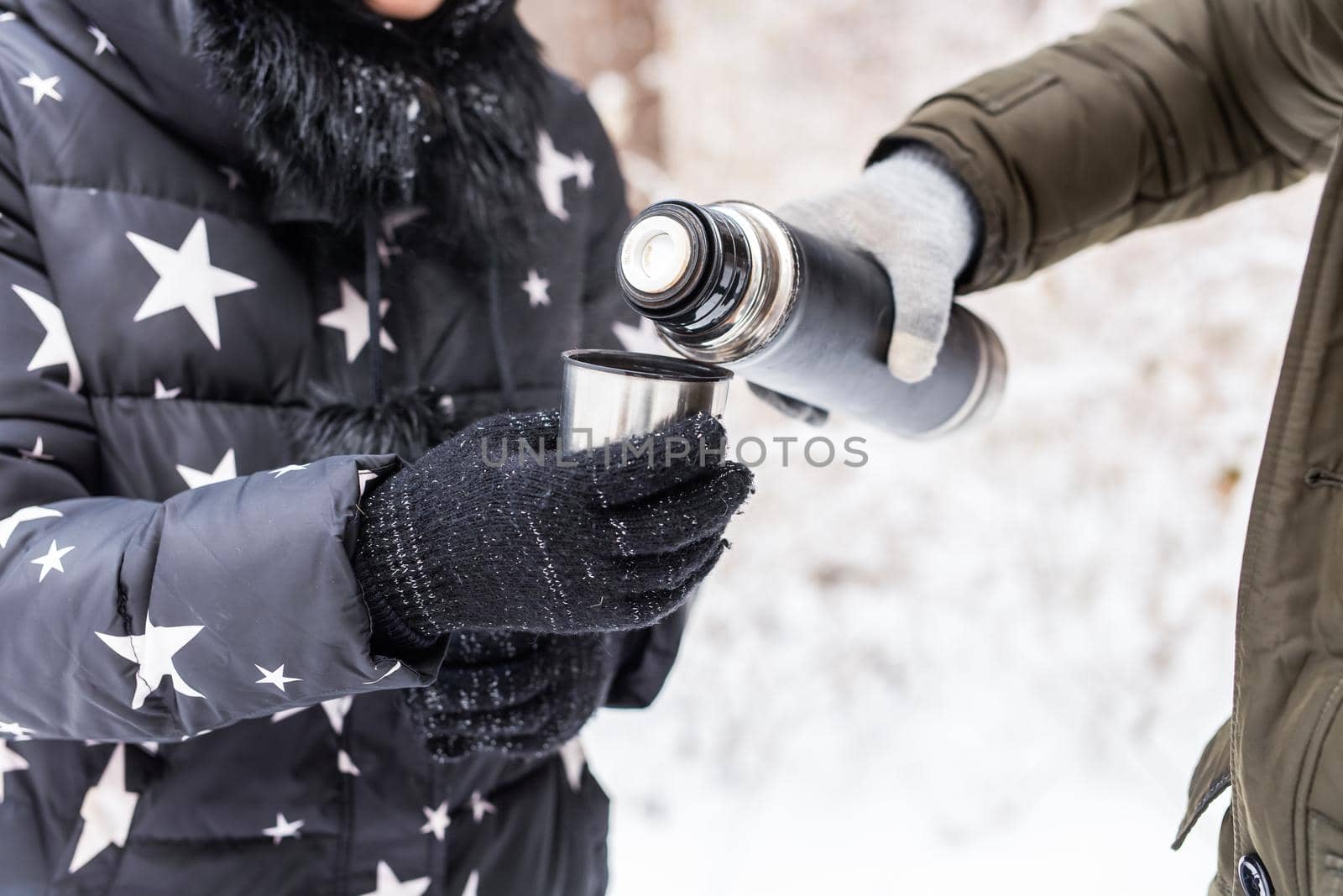 Thermos and cold season concept - A woman pours a hot drink. Couple on a winter holiday by Satura86
