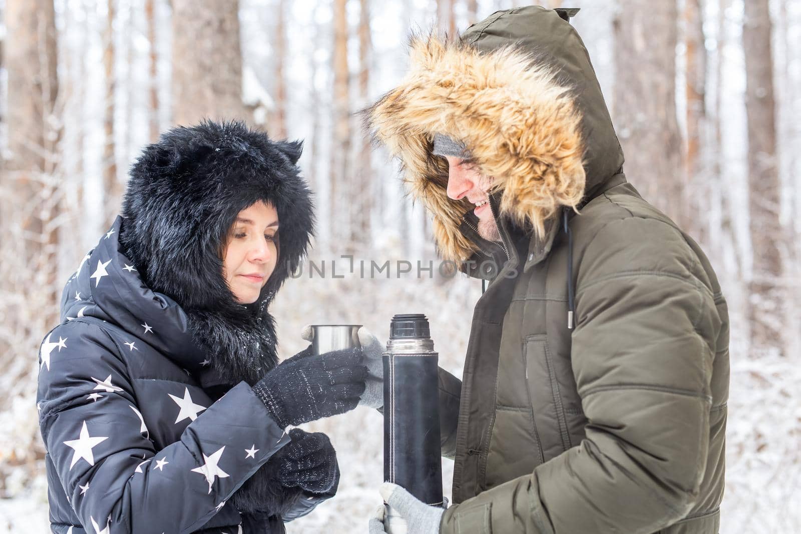 Season and walk concept - Happy couple drinking hot tea in winter forest by Satura86