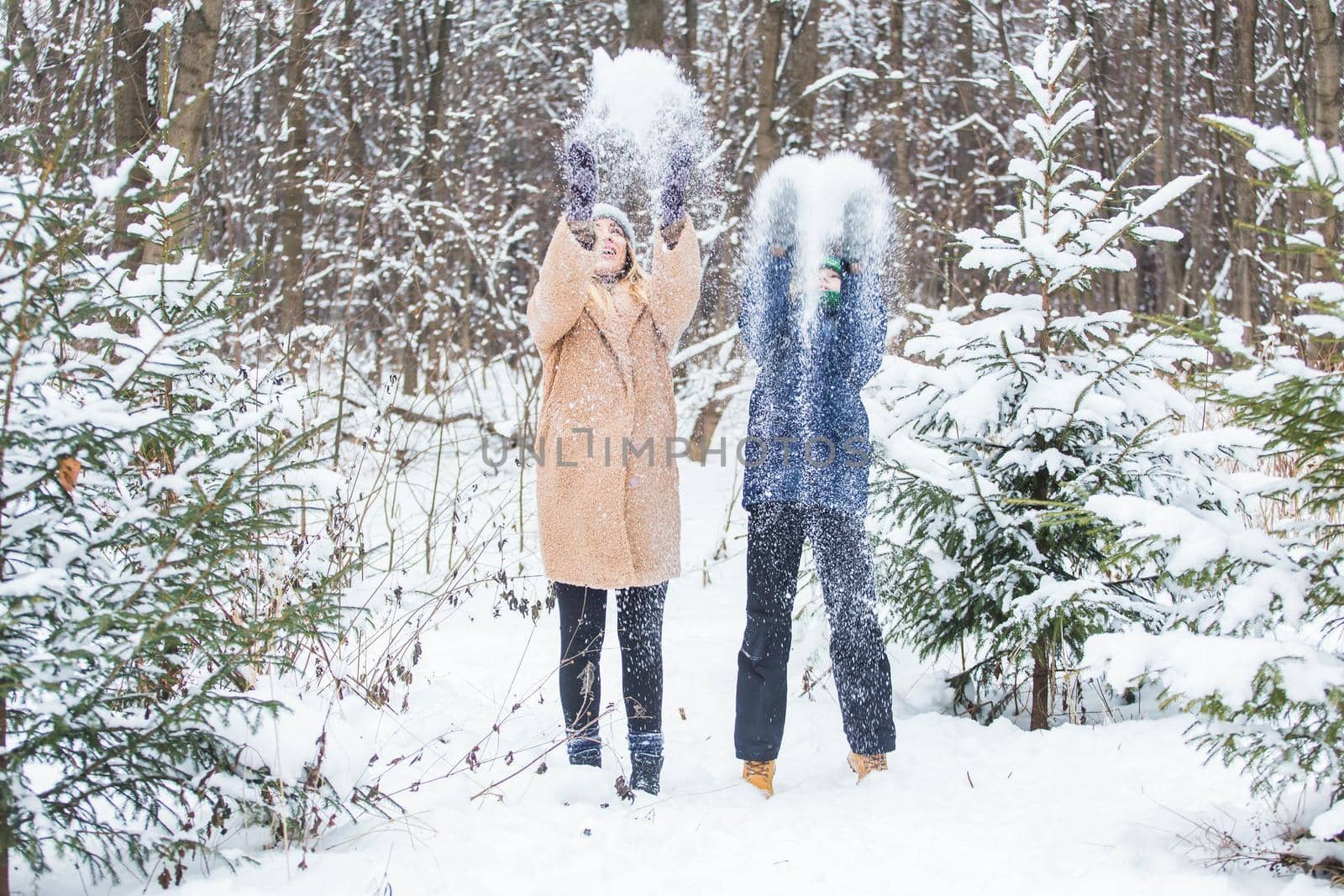 Parenting, fun and season concept - Happy mother and son having fun and playing with snow in winter forest.