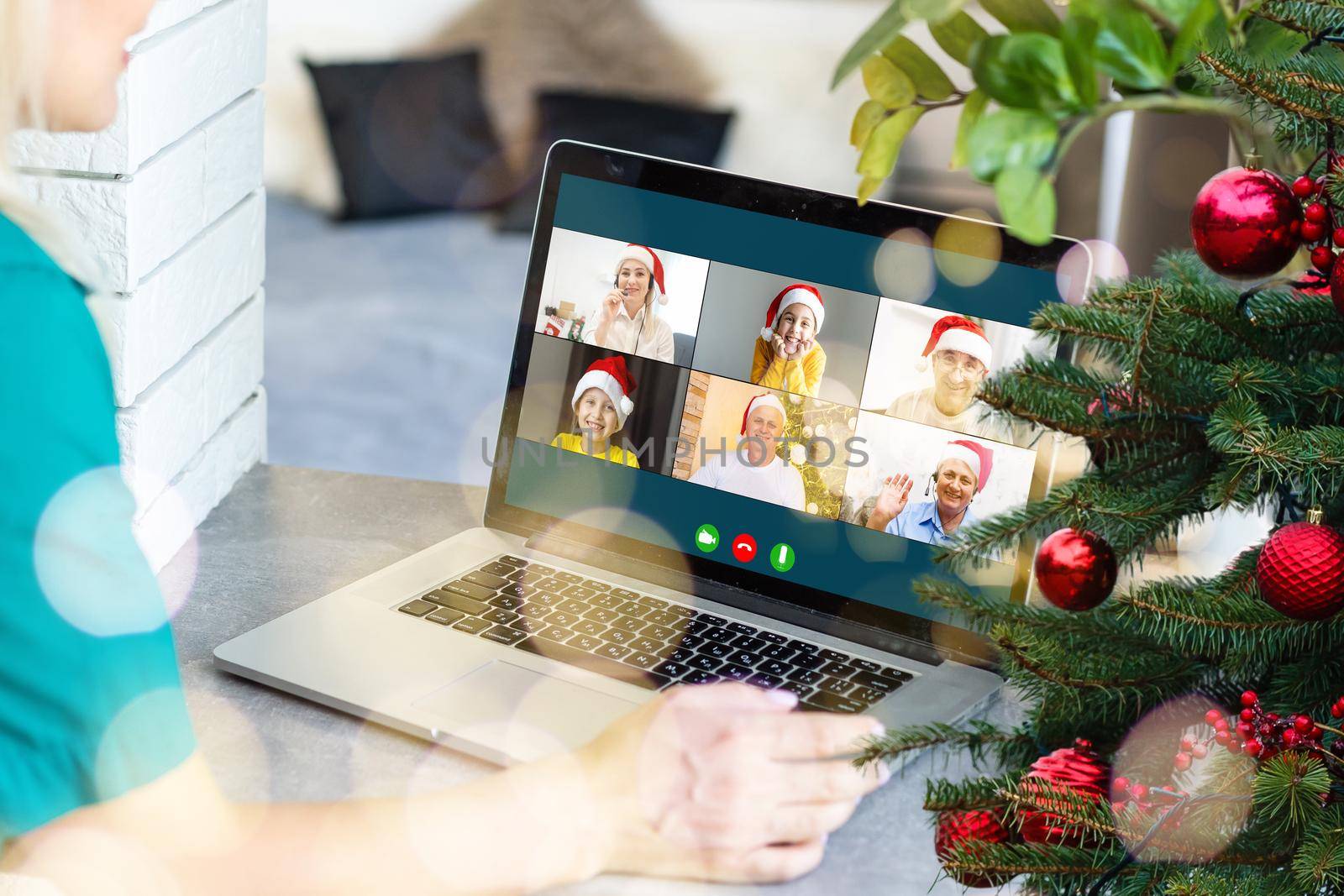 Christmas greetings online. a woman in a white sweater and red Santa hat uses a laptop to make video calls to friends, parents, and for online shopping by Andelov13