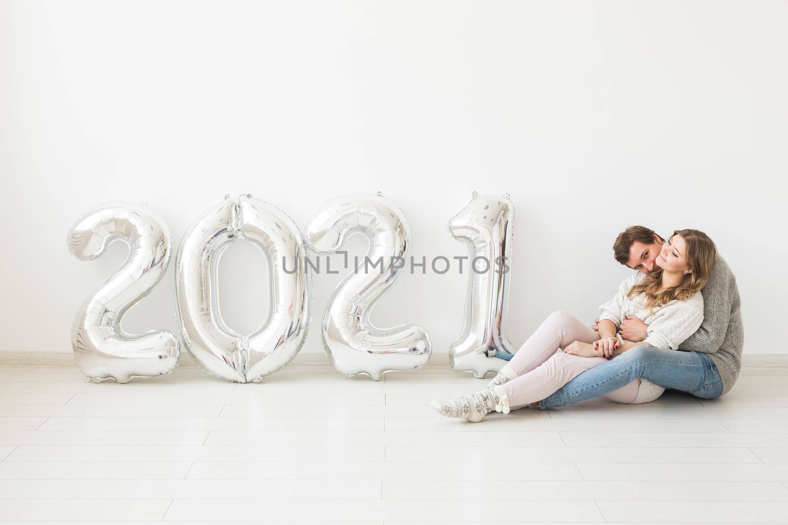 Holidays, festive and party concept - Happy loving couple holds silver 2021 balloons on white background. New Year celebration. by Satura86