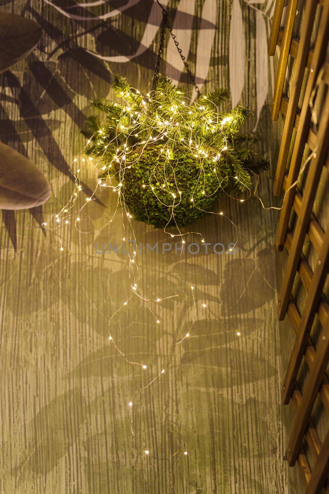 Pots with plants hanging on wall in the interior with yellow garlands. Holiday interior decor.