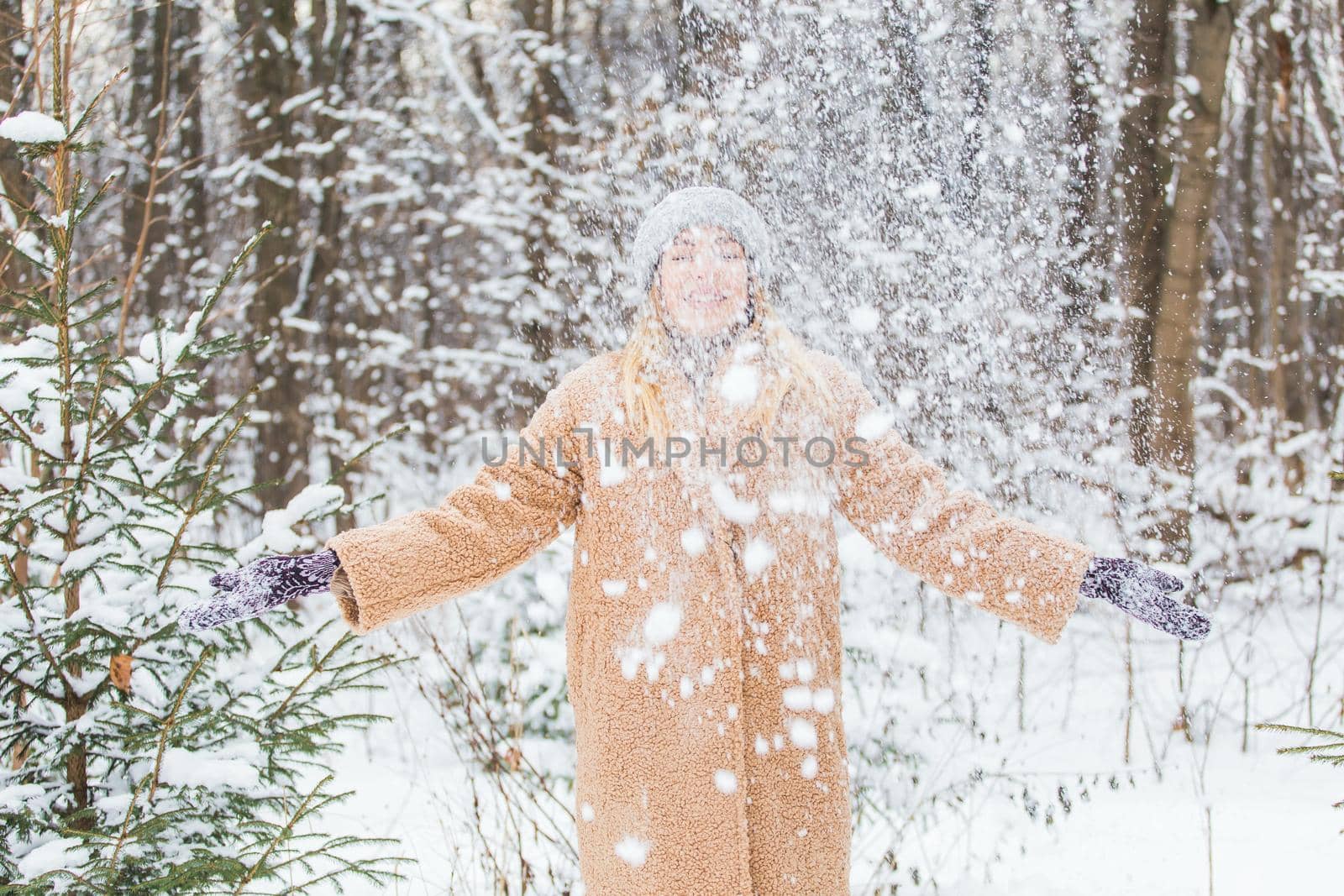 Young woman throwing snow in the air at sunny winter day, she is happy and fun