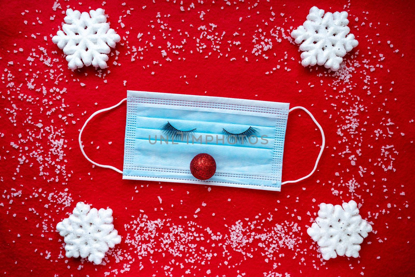 Protective medical face mask with eyes and red nose, christmas snowflakes on red background. by Matiunina