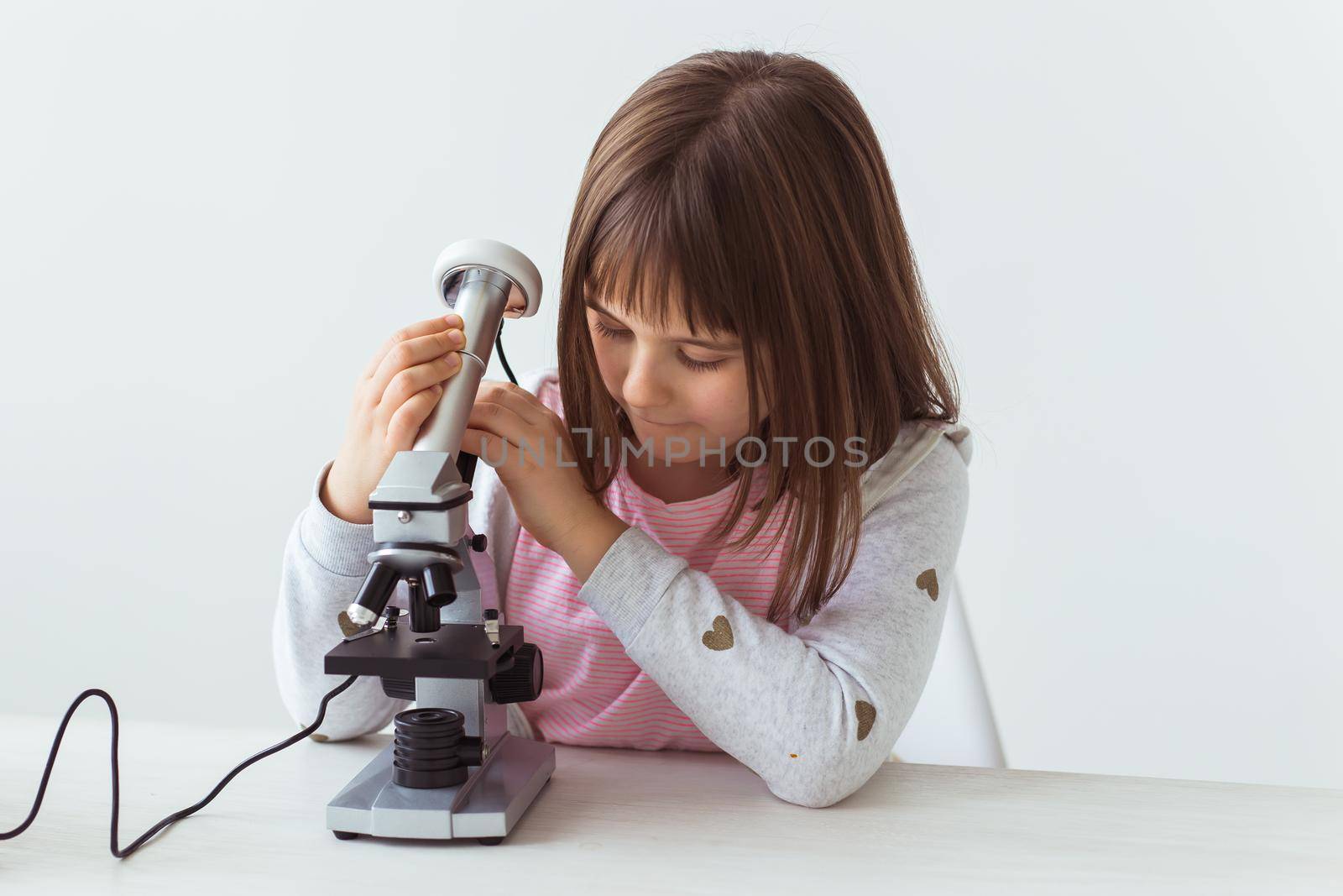 Schoolgirl using microscope in science class. Technologies, lessons and children concept. by Satura86