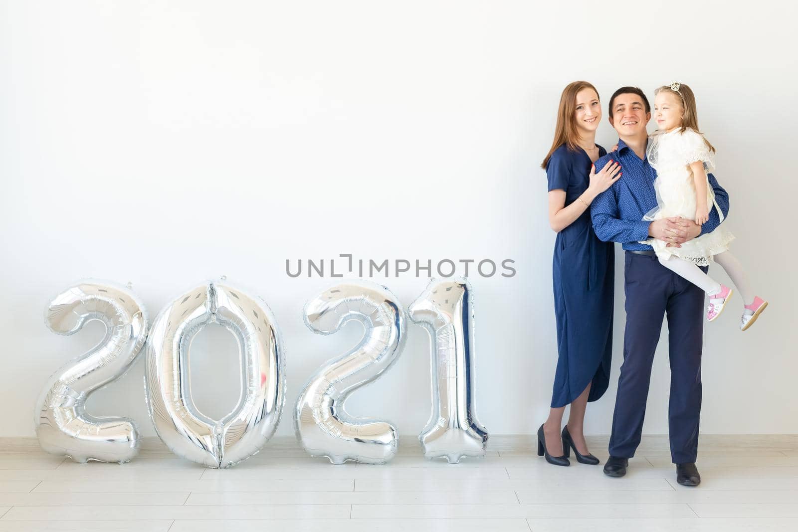 Young happy family mother and father and daughter standing near balloons shaped like numbers 2021 on white background. New year, Christmas, holiday by Satura86