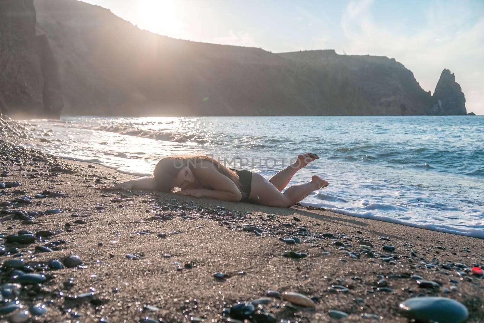 Selective focus. Happy carefree sensual woman with long hair in black swimwear posing at sunset beach. Silhouette of young beautiful playful positive woman outdoor. Summer vacation and trip concept by panophotograph