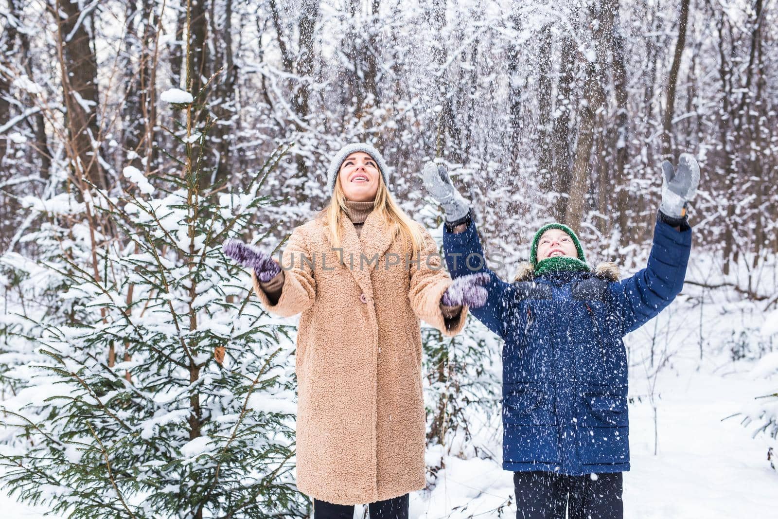 Parenting, fun and season concept - Happy mother and son having fun and playing with snow in winter forest.