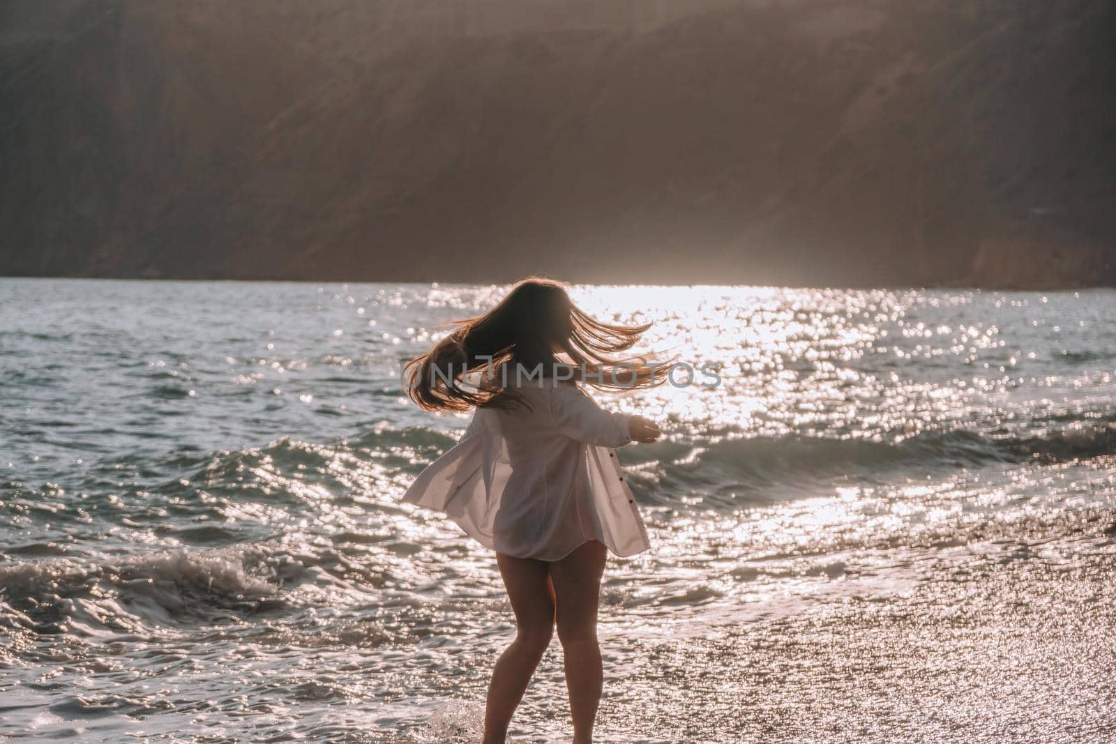 Selective focus. Happy carefree sensual woman with long hair in black swimwear posing at sunset beach. Silhouette of young beautiful playful positive woman outdoor. Summer vacation and trip concept.