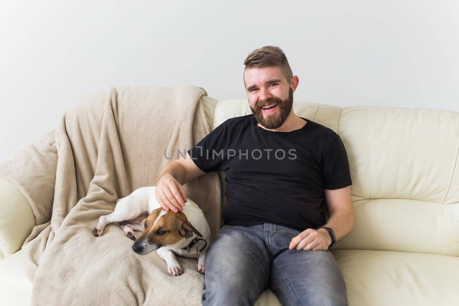 Attractive cheerful Caucasian male in casual t shirt sitting on couch favourite pet. Happy bearded man with his jack russell terrier. Pet's owner concept. by Satura86