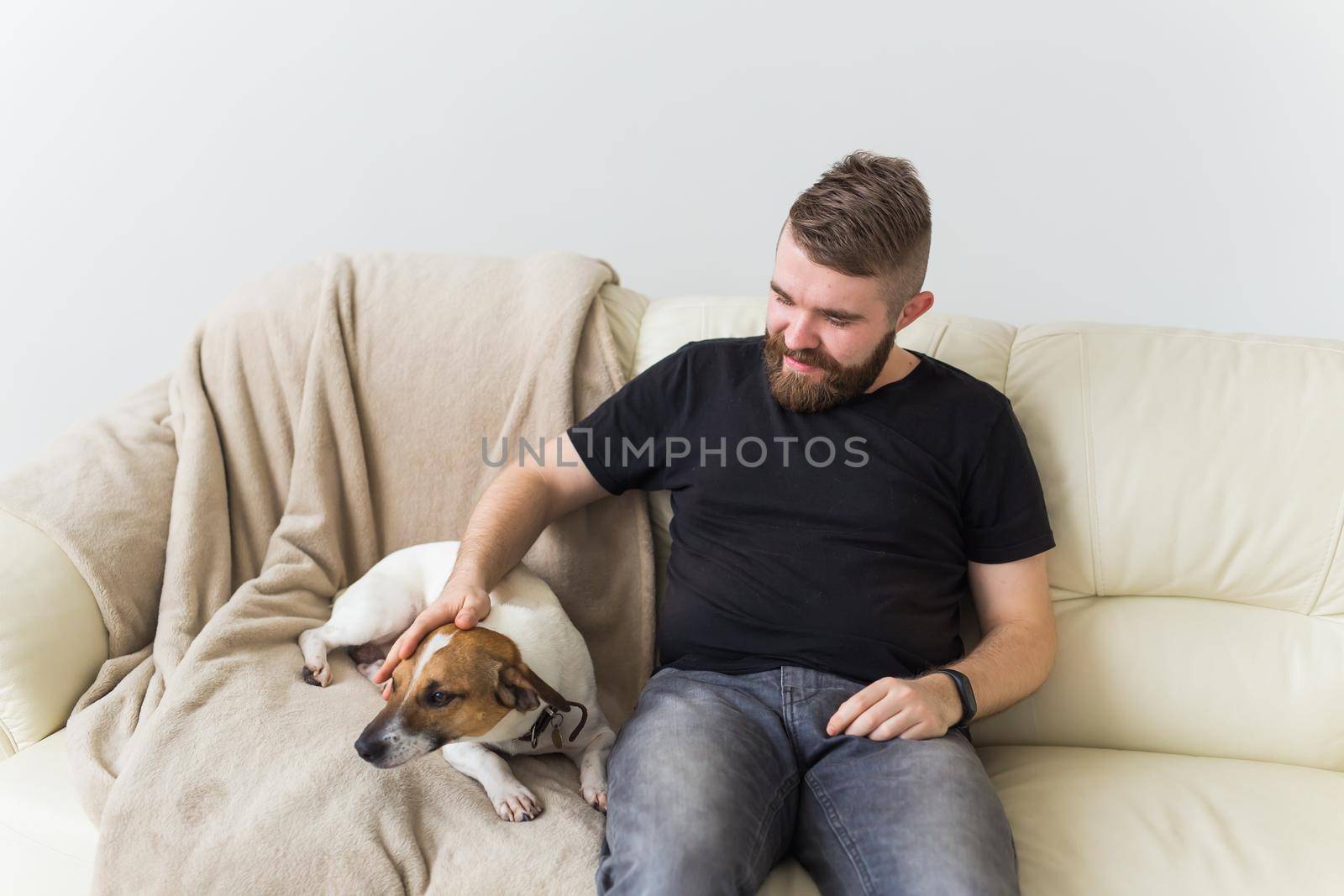 Attractive cheerful Caucasian male in casual t shirt sitting on couch favourite pet. Happy bearded man with his jack russell terrier. Pet's owner concept
