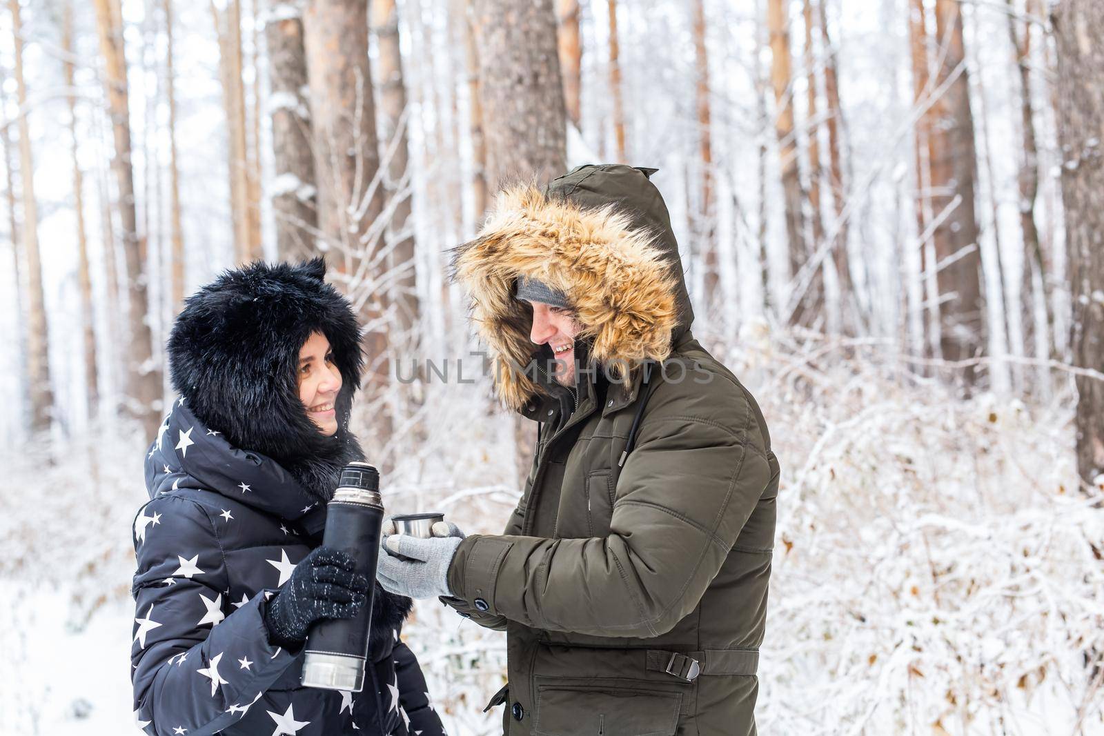 Young couple in love drink a hot drink from a thermos and enjoy winter nature. by Satura86