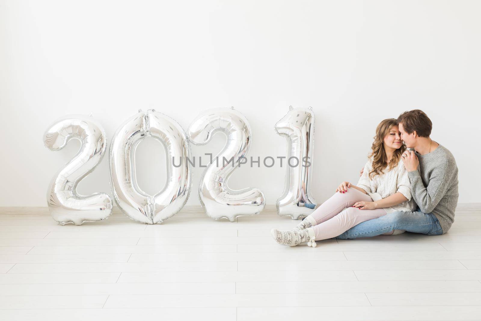 Holidays, festive and party concept - Happy loving couple holds silver 2021 balloons on white background. New Year celebration