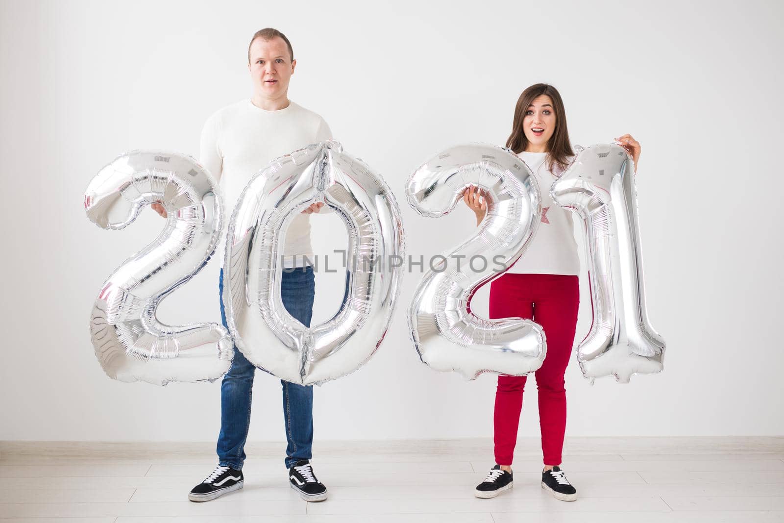 New 2021 Year is coming concept - Happy young man and woman are holding silver colored numbers indoors