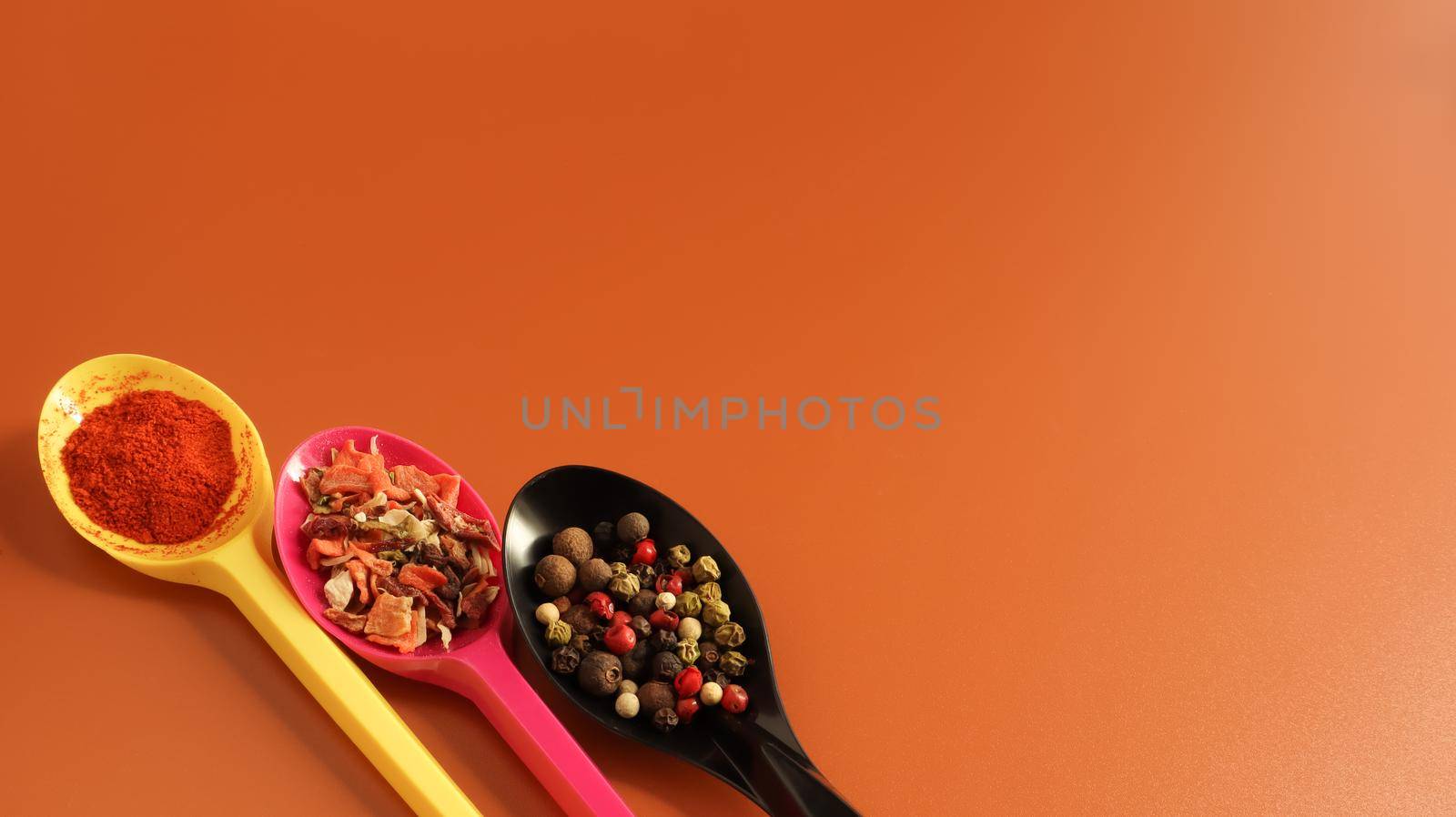 Various spices in plastic spoons on a brown background. Copy space. A mixture of peppers, red smoked paprika, seasoning twelve vegetables