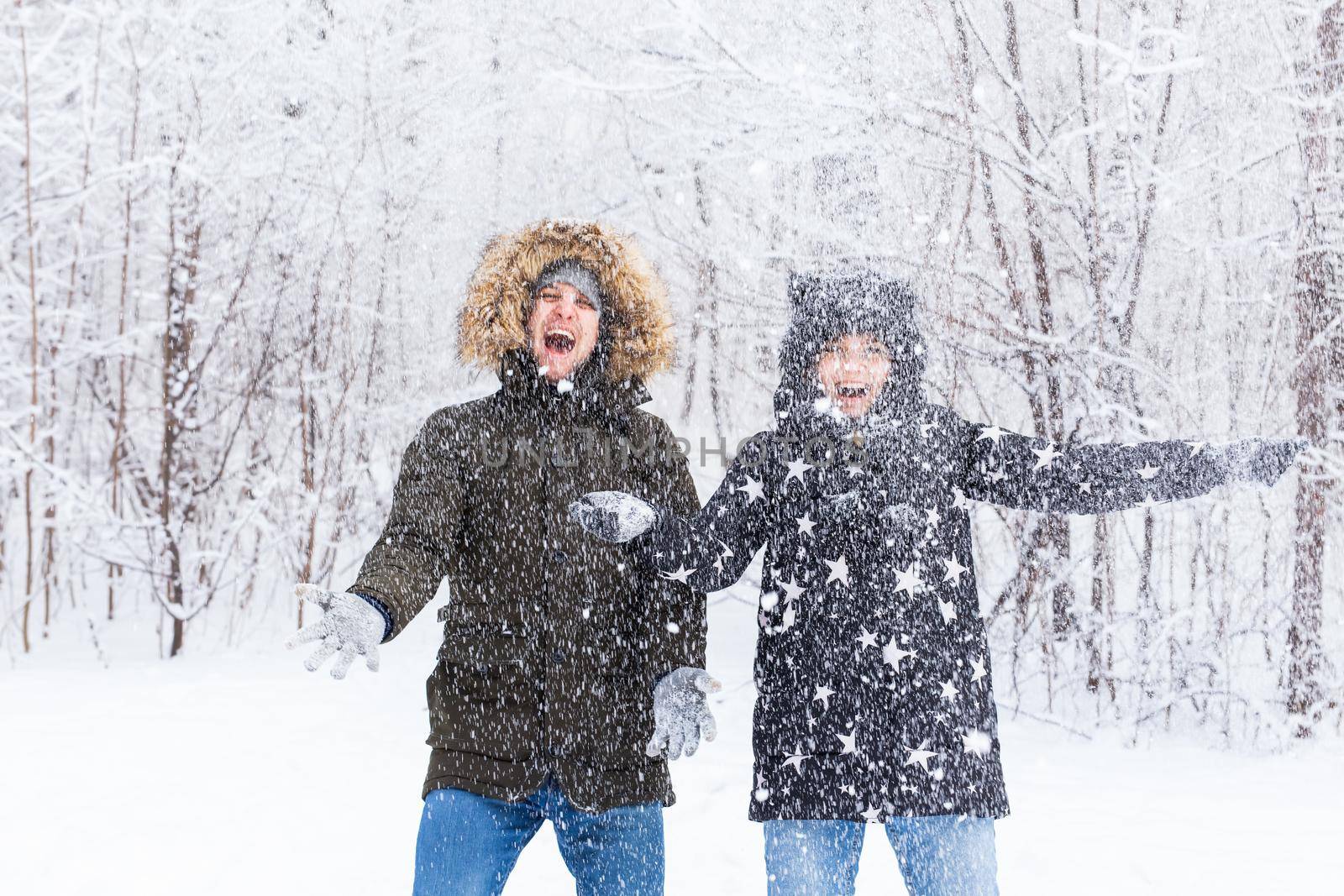 Young couple in a bright clothes throw up a snow in a winter forest