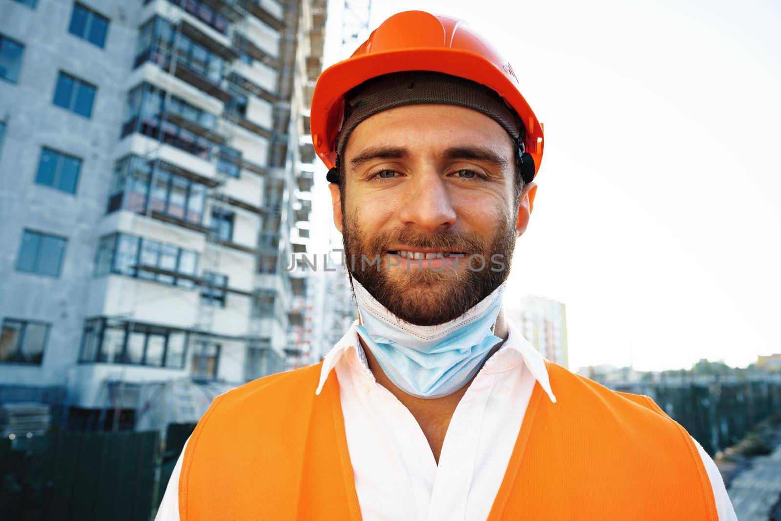 Portrait of man builder in workwear and hardhat wearing medical mask, close up photo