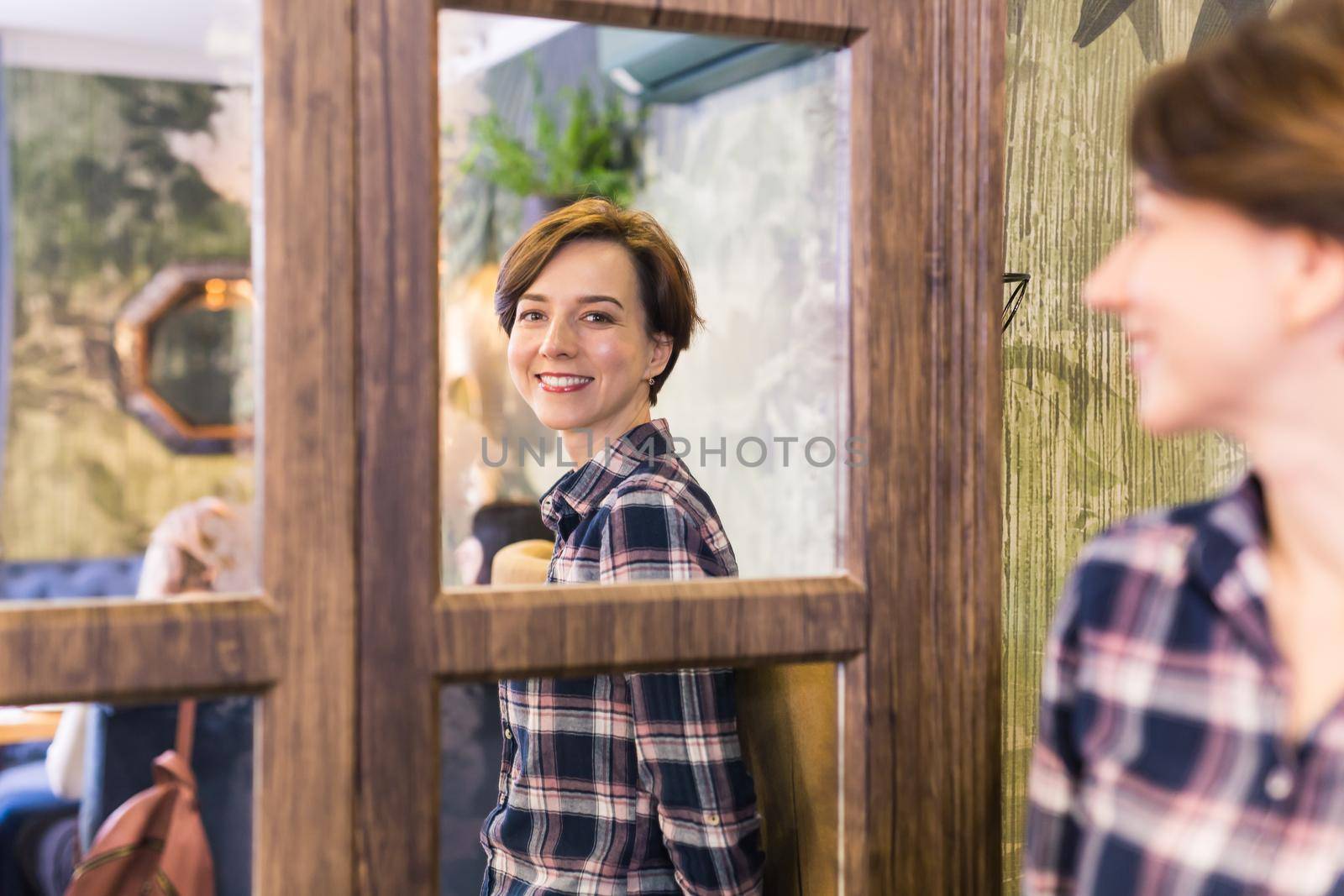 Young woman looking in a mirror. The mirror reflects her smiling face. Natural beauty and female.