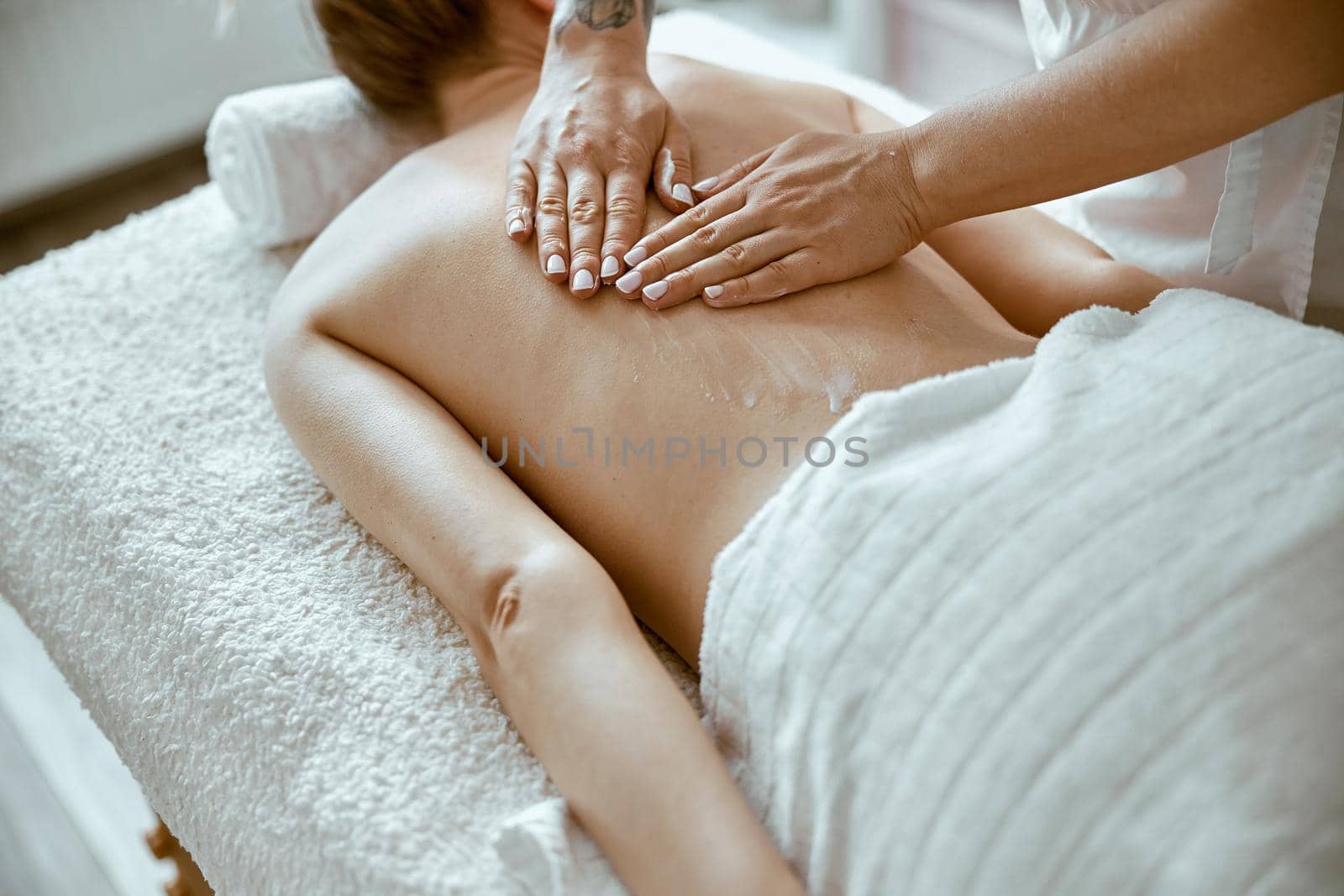 confident female specialist is doing relaxing body massage for beautyful slim caucasian lady at minimalistic spa salon