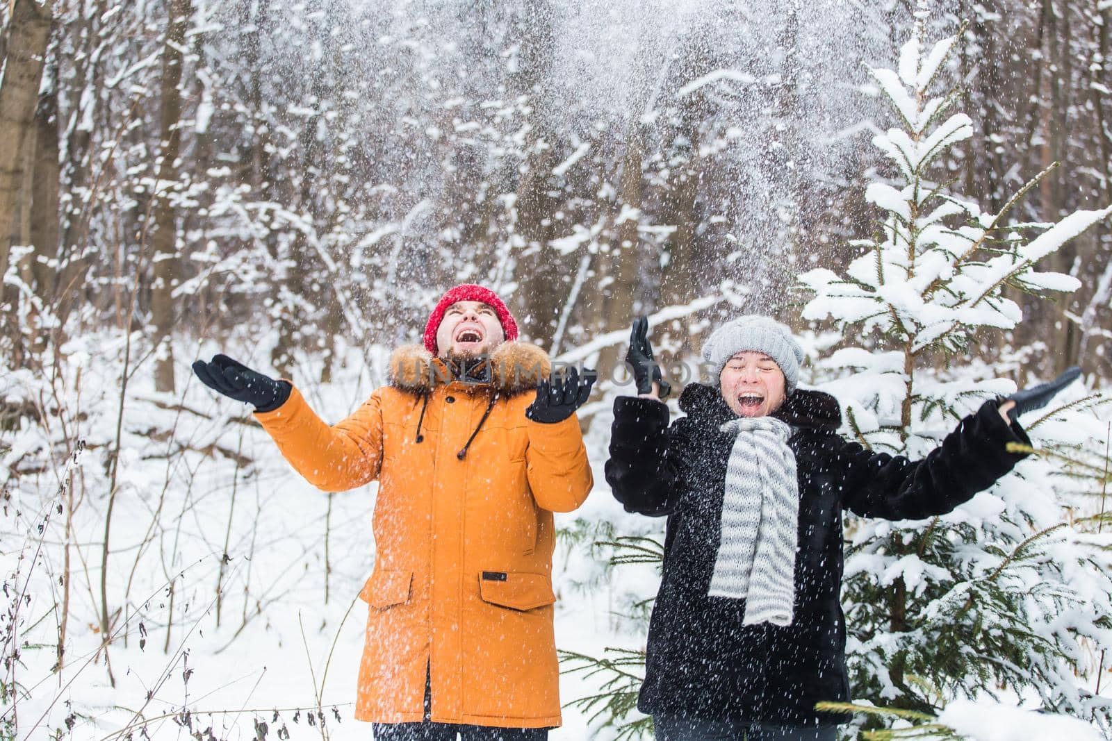 Love, season, friendship and people concept - happy young man and woman having fun and playing with snow in winter forest.