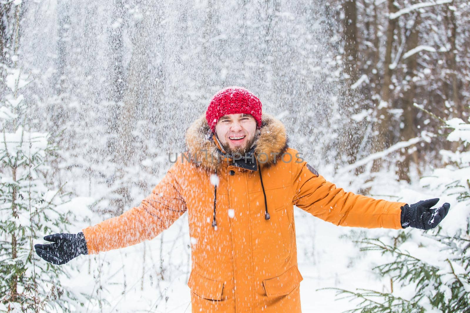 Young man throwing snow in winter forest. Guy having fun outdoors. Winter activities