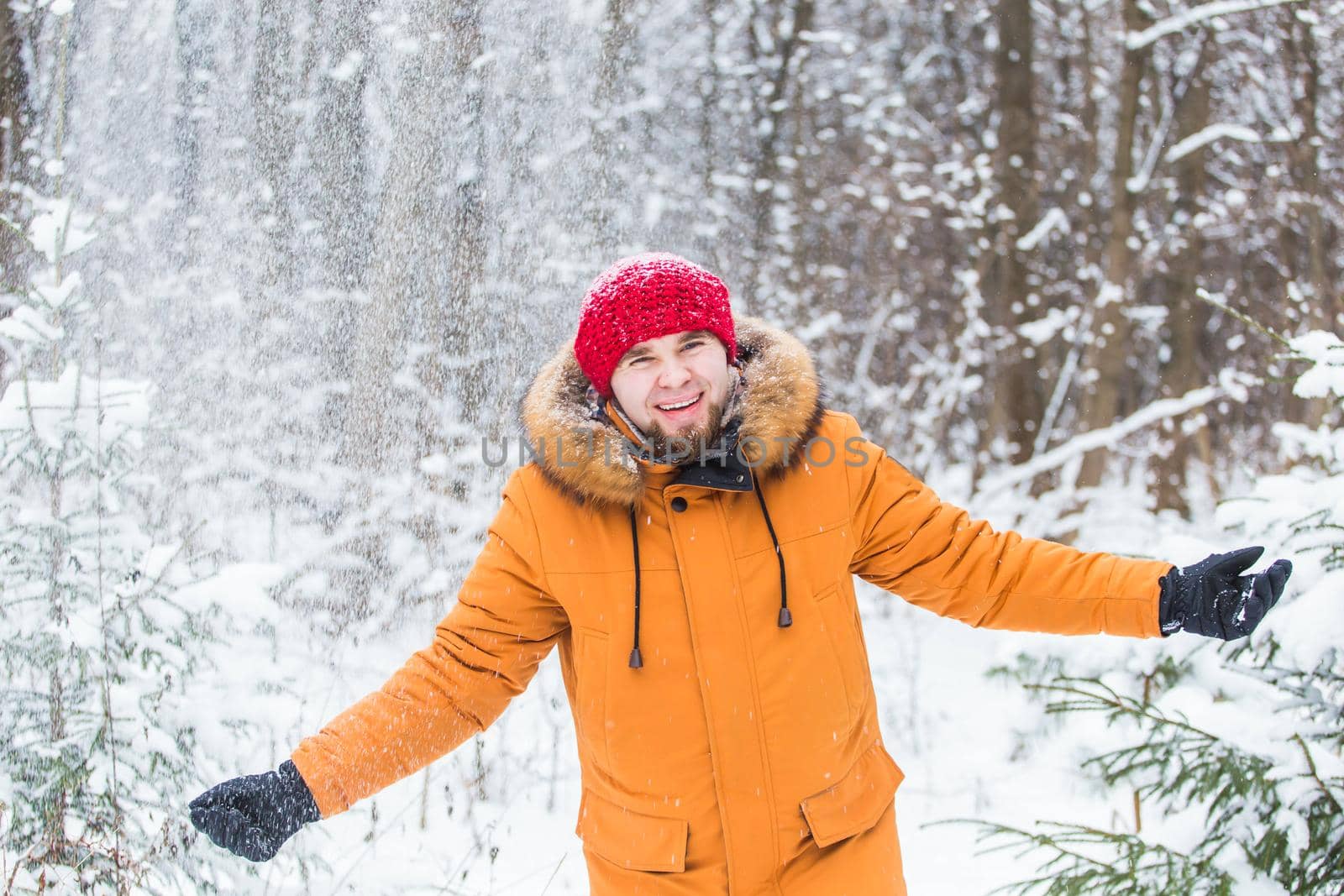 Young man throwing snow in winter forest. Guy having fun outdoors. Winter activities