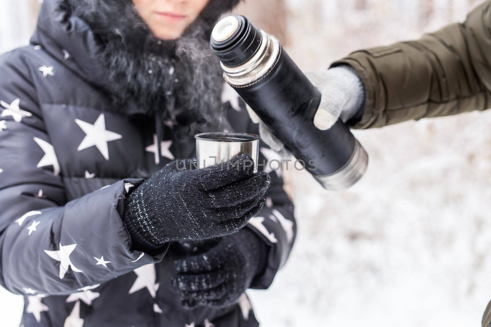 Thermos and cold season concept - A woman pours a hot drink. Couple on a winter holiday.
