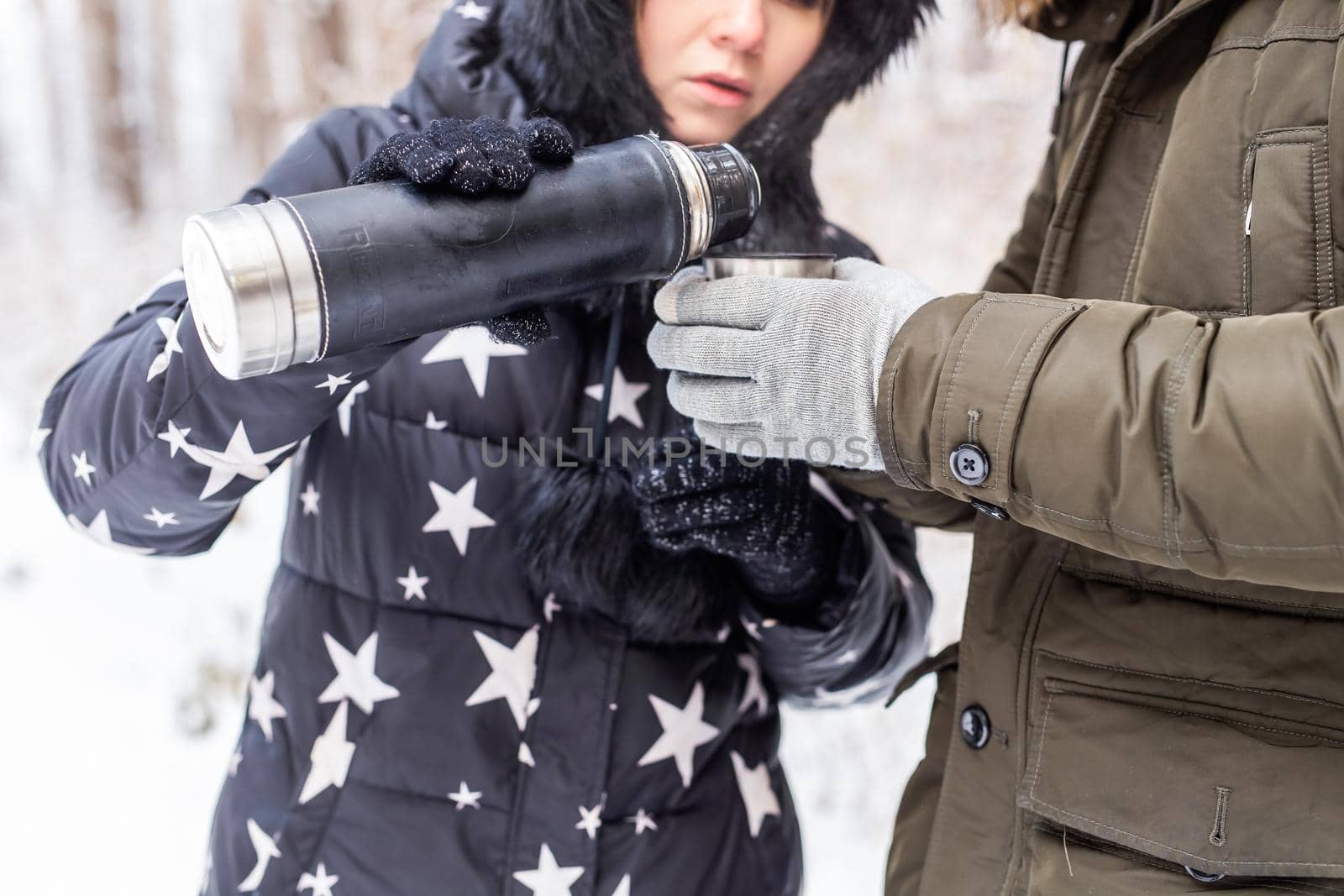 Thermos and cold season concept - A woman pours a hot drink. Couple on a winter holiday.