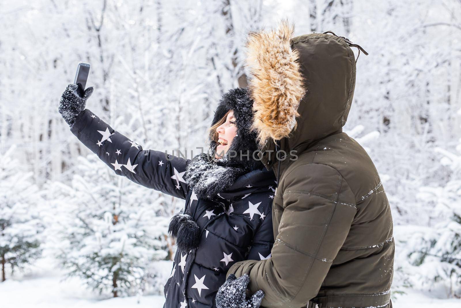 Technologies and relationship concept - Happy smiling couple taking a selfie in a winter forest outside by Satura86