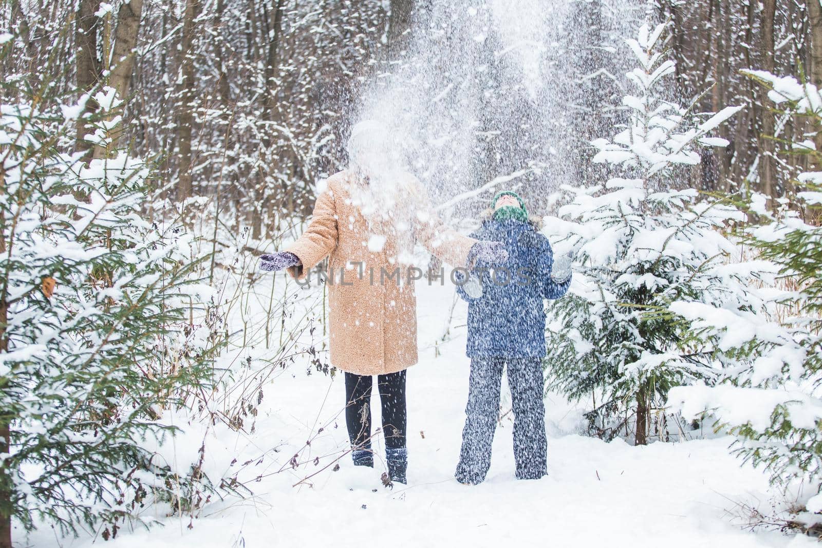 Parenting, fun and season concept - Happy mother and son having fun and playing with snow in winter forest.