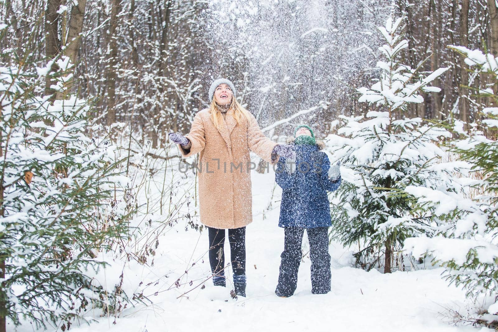 Parenting, fun and season concept - Happy mother and son having fun and playing with snow in winter forest.