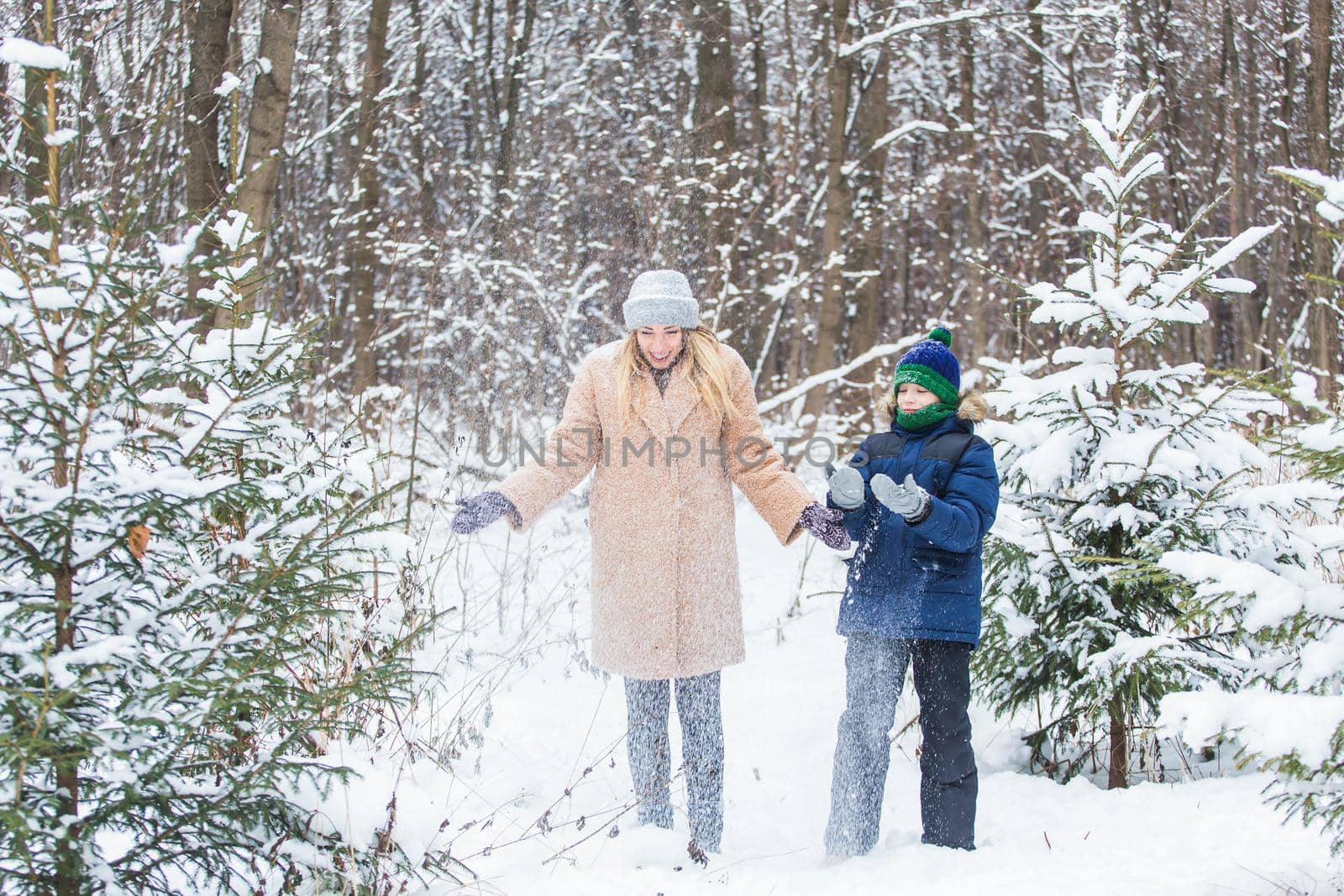 Parenting, fun and season concept - Happy mother and son having fun and playing with snow in winter forest by Satura86