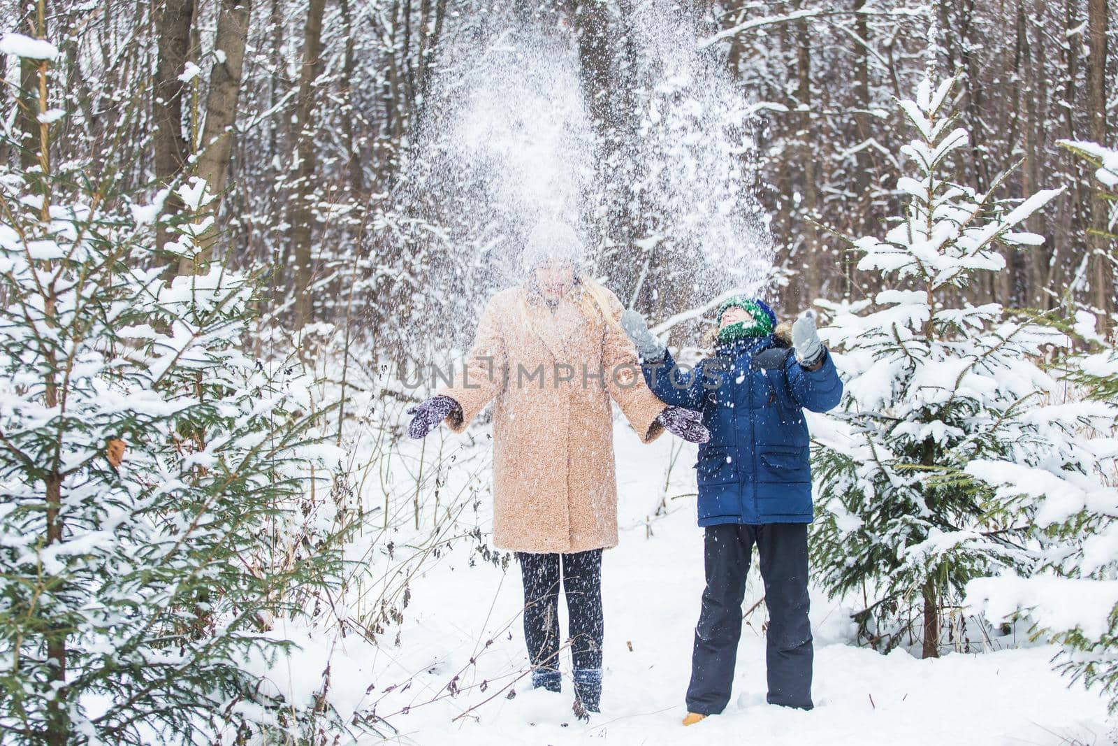 Parenting, fun and season concept - Happy mother and son having fun and playing with snow in winter forest.