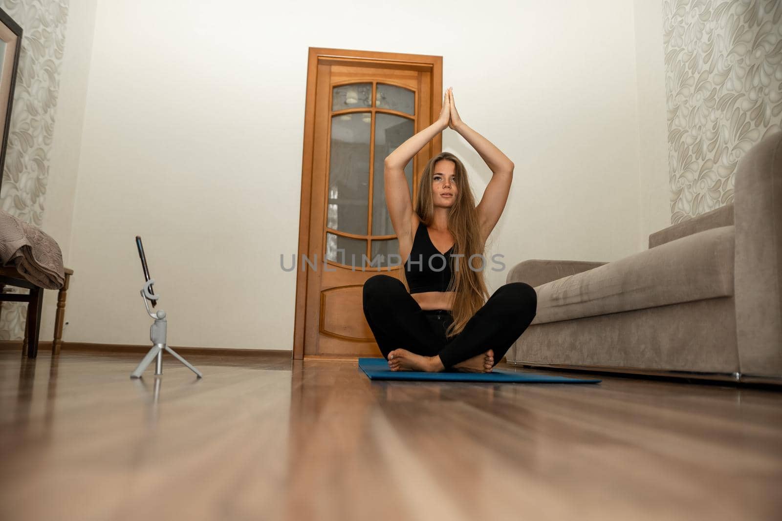 Young woman with long hair, fitness instructor in black sportswear, doing stretching and pilates on yoga mat at home. Female fitness yoga routine concept. Healthy lifestyle harmony and meditation
