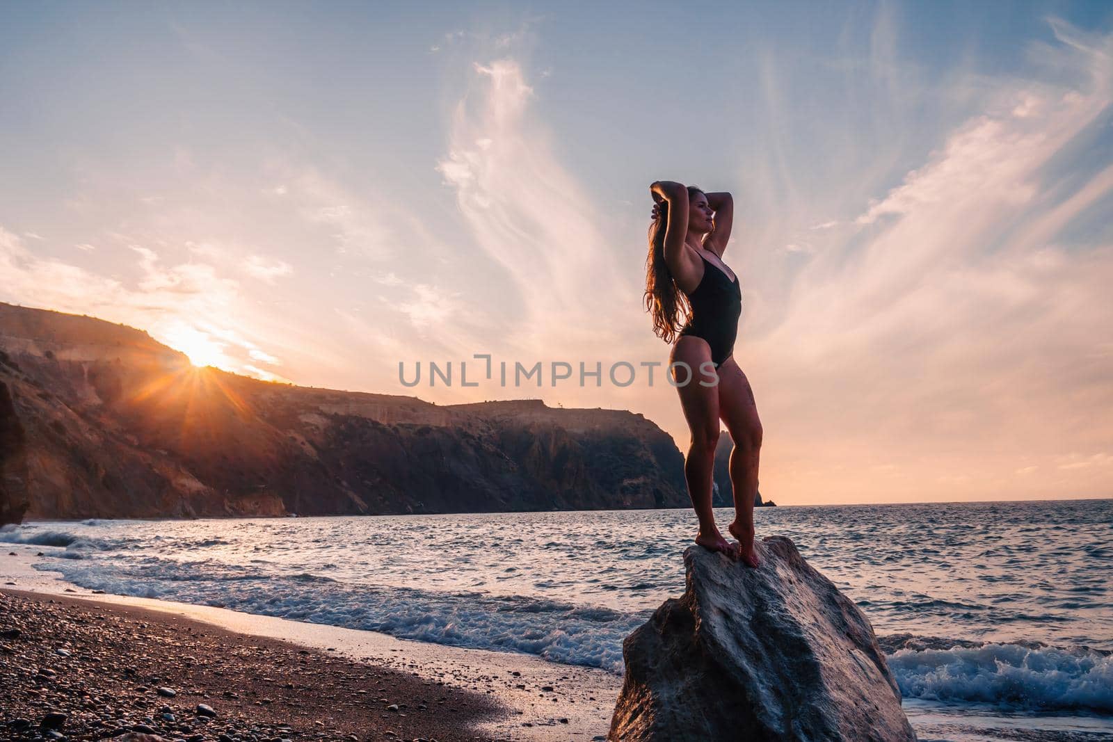 Selective focus. Happy carefree sensual woman with long hair in black swimwear posing at sunset beach. Silhouette of young beautiful playful positive woman outdoor. Summer vacation and trip concept.