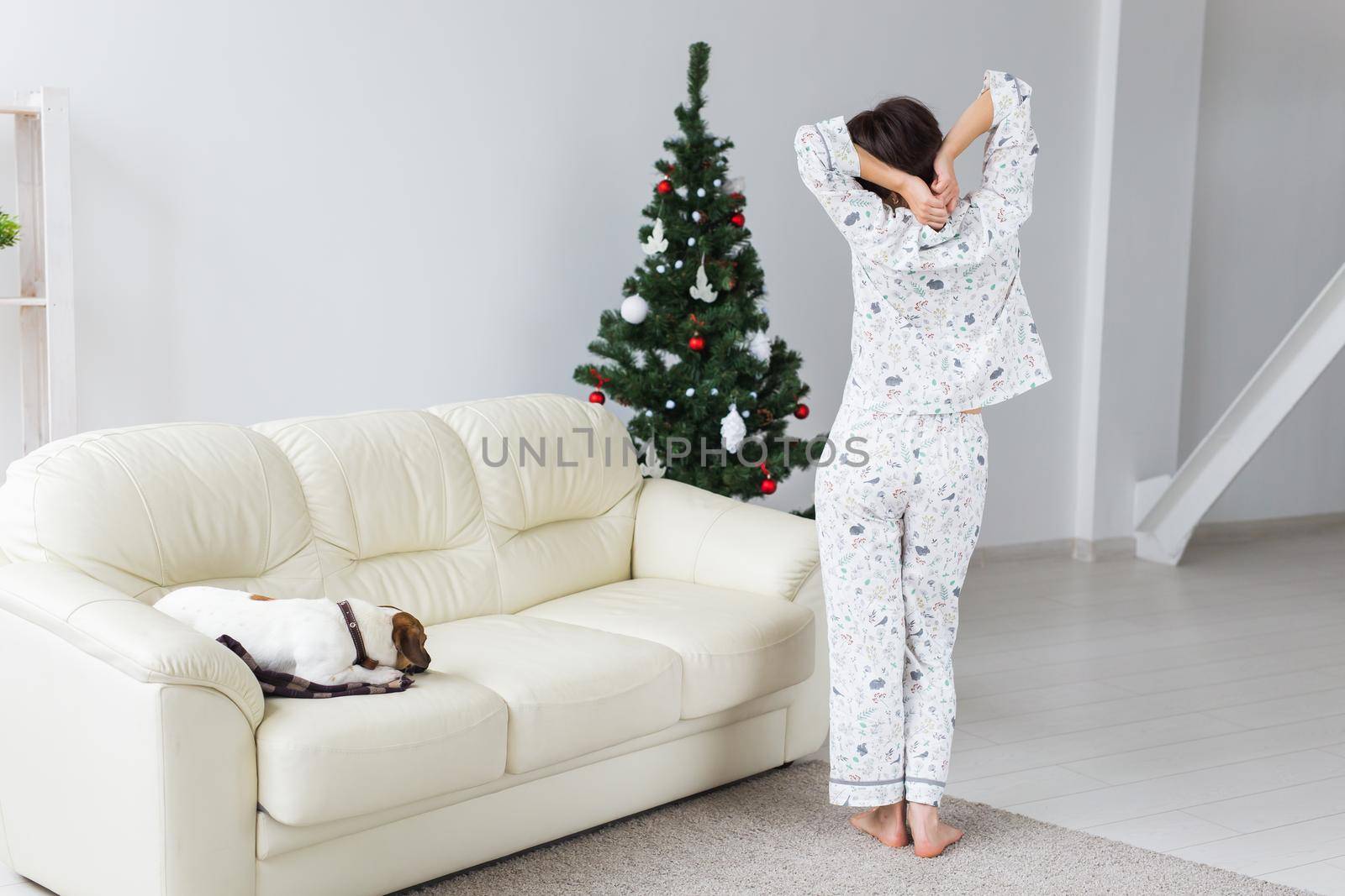 Happy young woman with lovely dog in living room with christmas tree. Holidays.