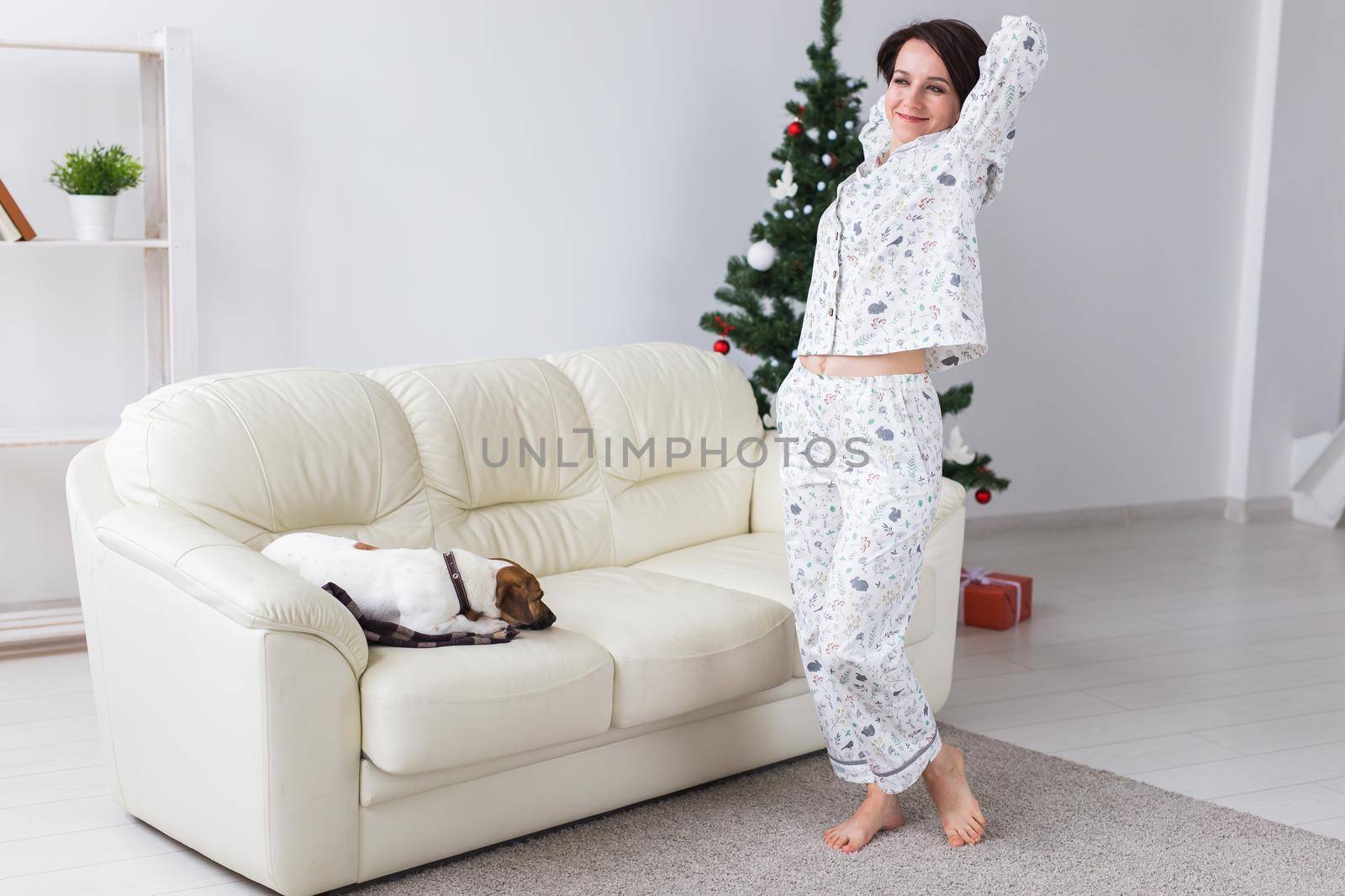 Happy young woman with lovely dog in living room with christmas tree. Holidays.