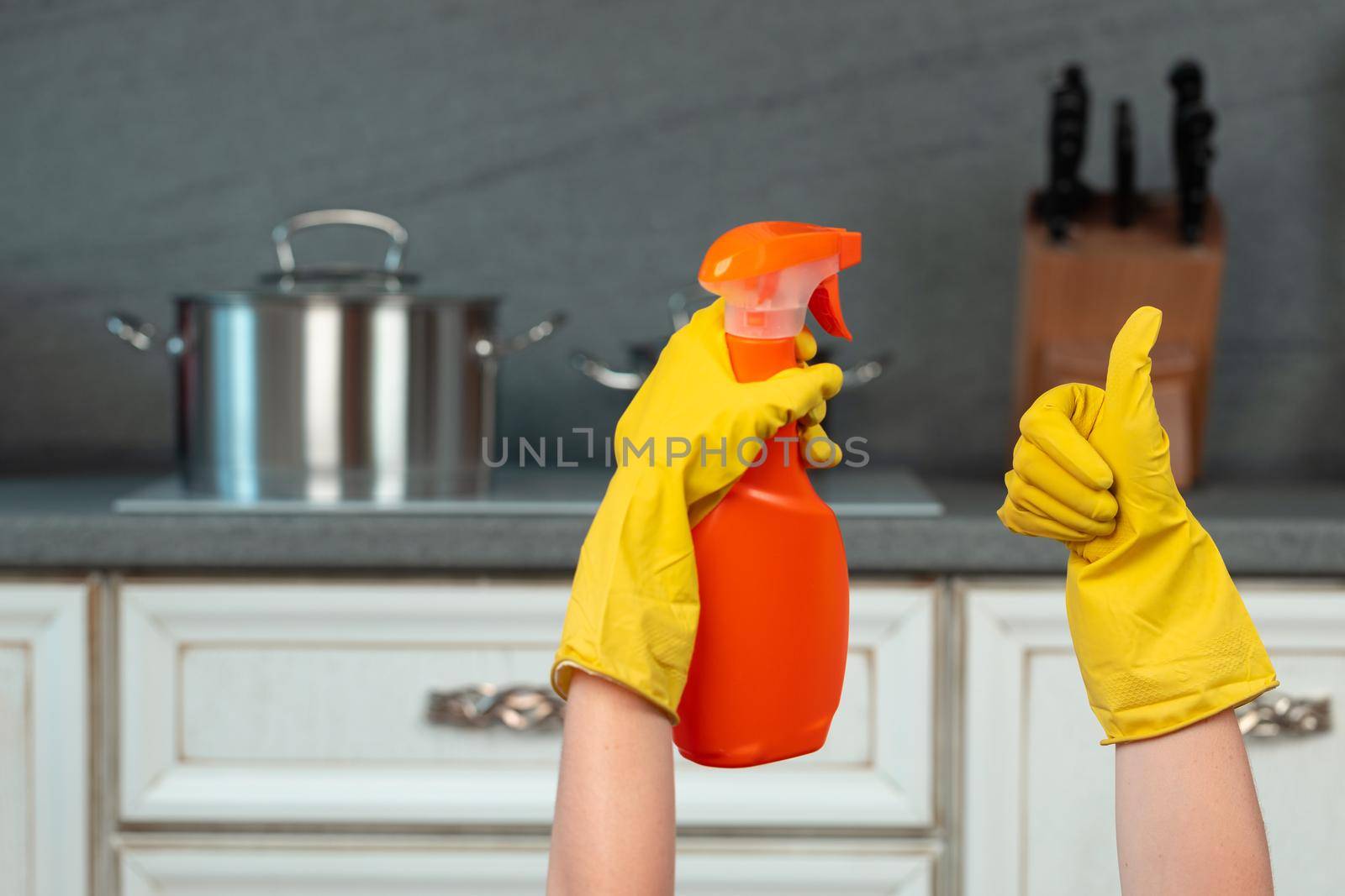Hands in yellow gloves against blurred kitchen background. Housekeeping concept
