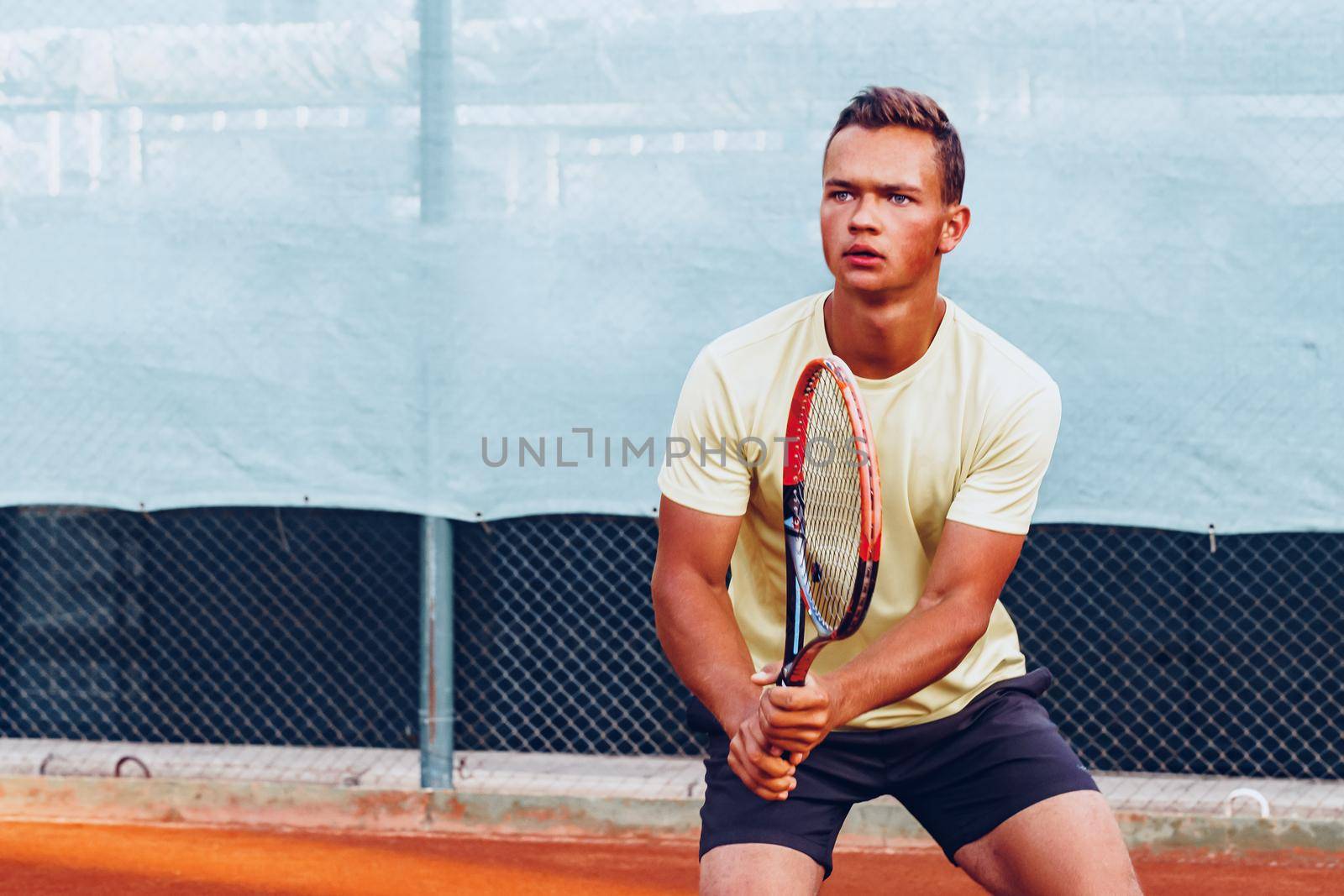 Young handsome man playing tennis on the clay tennis court