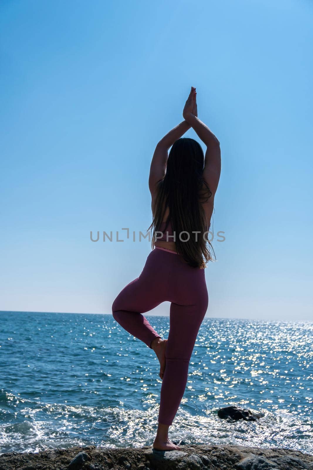 Young woman with long hair, fitness instructor in Sportswear Leggings and Tops, stretching before pilates, on a yoga mat near the sea on a sunny day, female fitness yoga routine concept by panophotograph