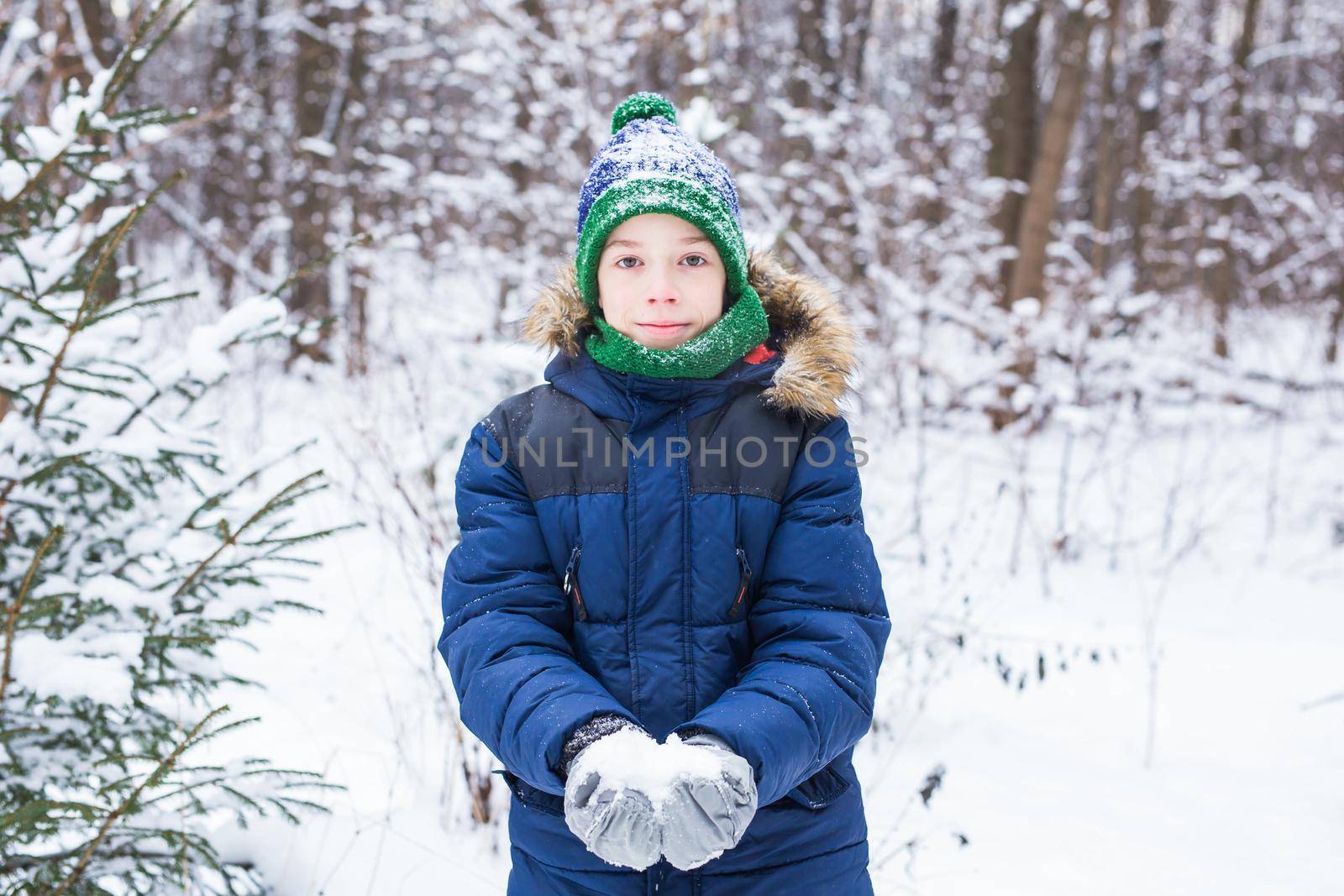 Young boy plays with snow, have fun, smiles. Teenager in winter park. Active lifestyle, winter activity, outdoor winter games, snowballs.